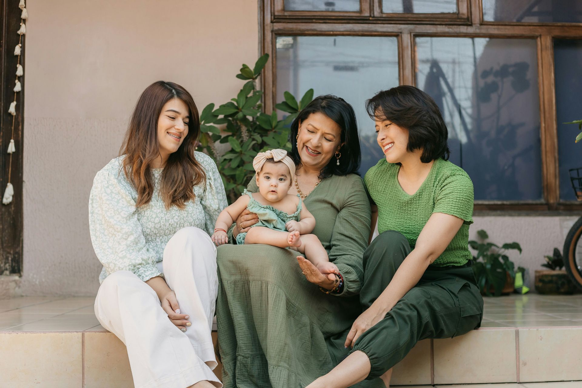 A group of women are sitting on a porch holding a baby.