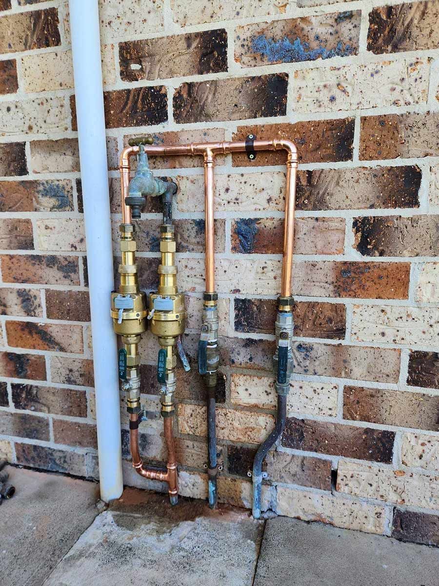 A Brick Wall With Copper Pipes Attached To It — Country 2 Coast Plumbing And Gas In Wauchope, NSW 
