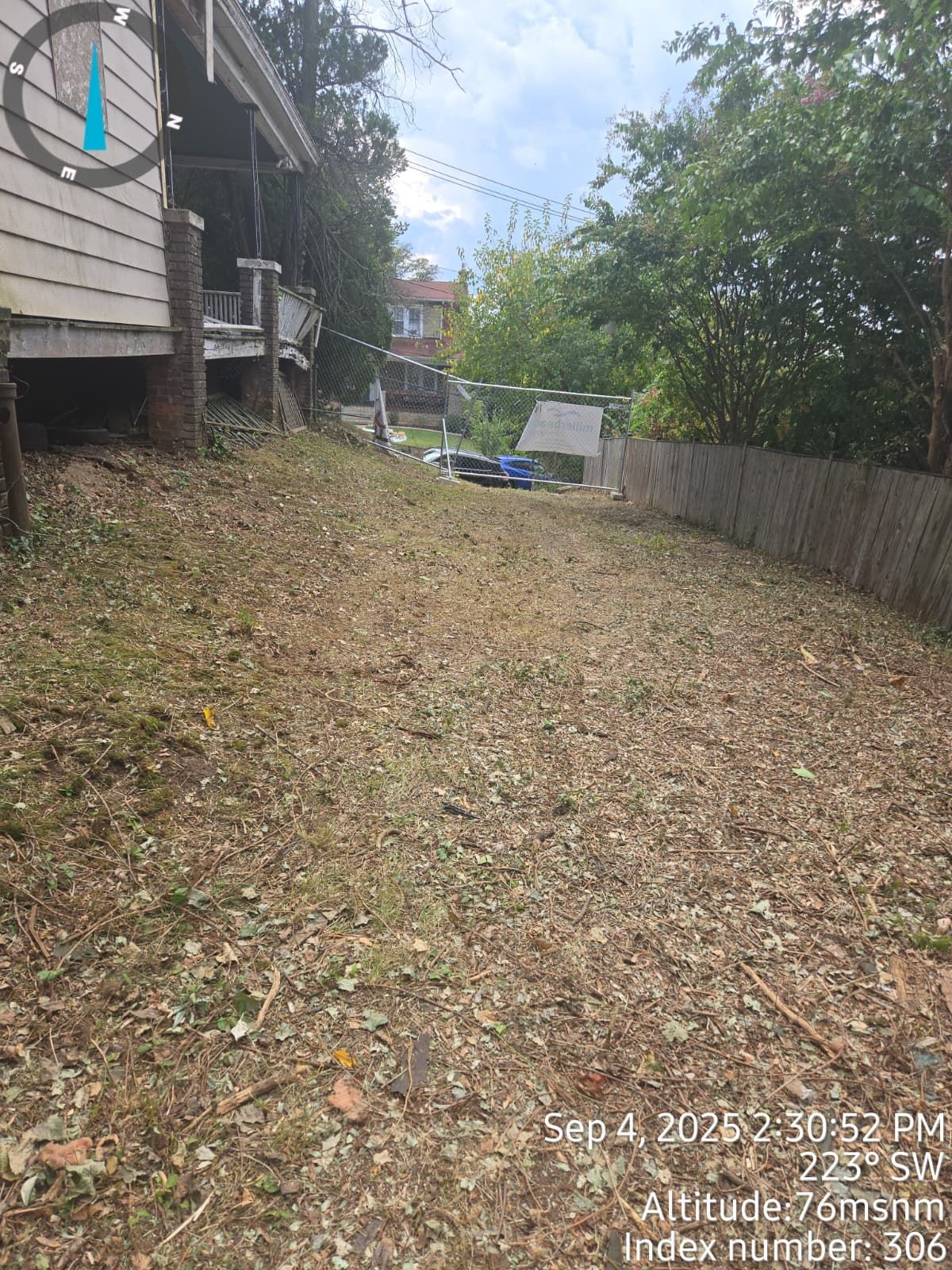 A yard covered in fallen leaves, trees and buildings on either side.