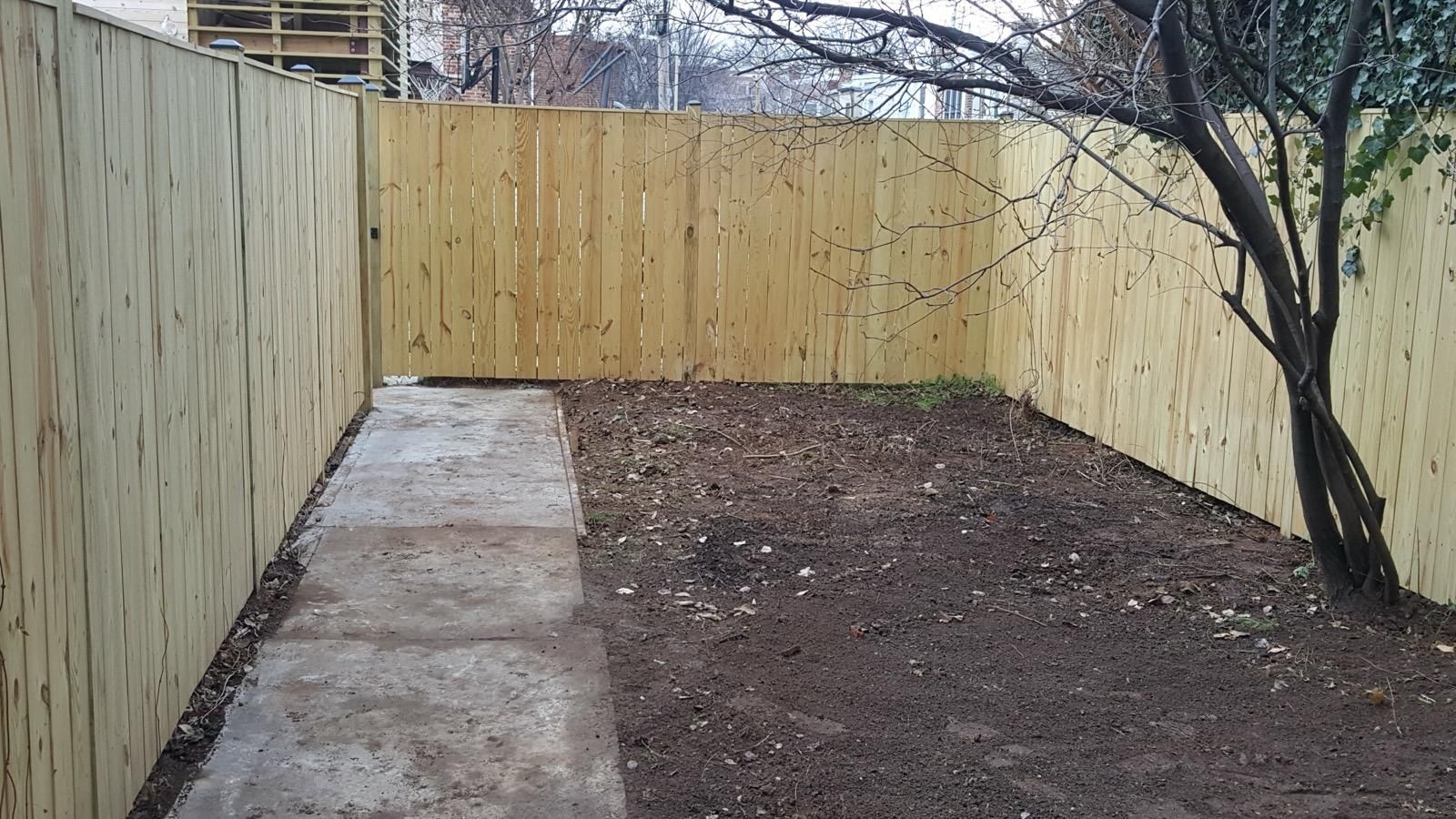 A wooden fence surrounds a concrete walkway in a backyard.