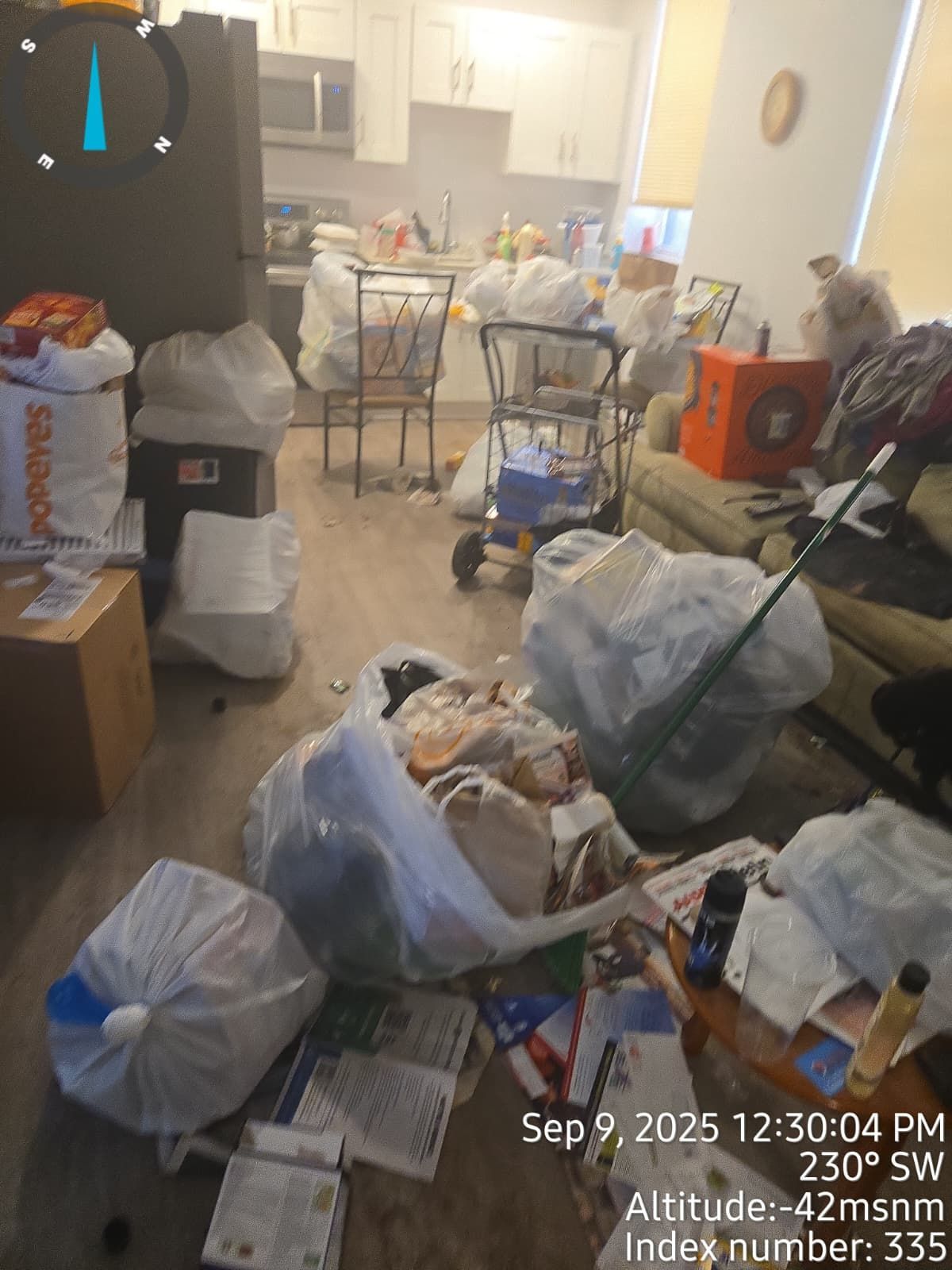 Cluttered kitchen interior with bags of trash, boxes, and debris scattered on the floor.