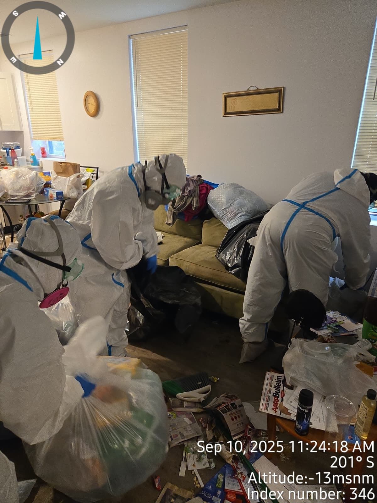 People in hazmat suits cleaning a cluttered room; date, time, and coordinates visible.