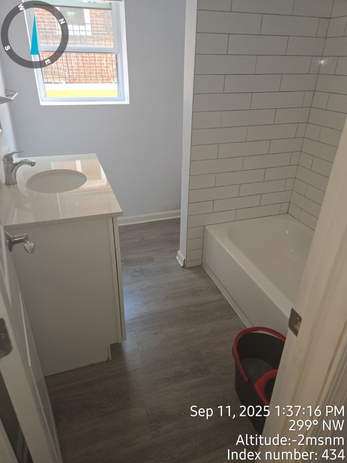 Bathroom with white vanity, gray floor, white tub, and white brick-like tile wall.