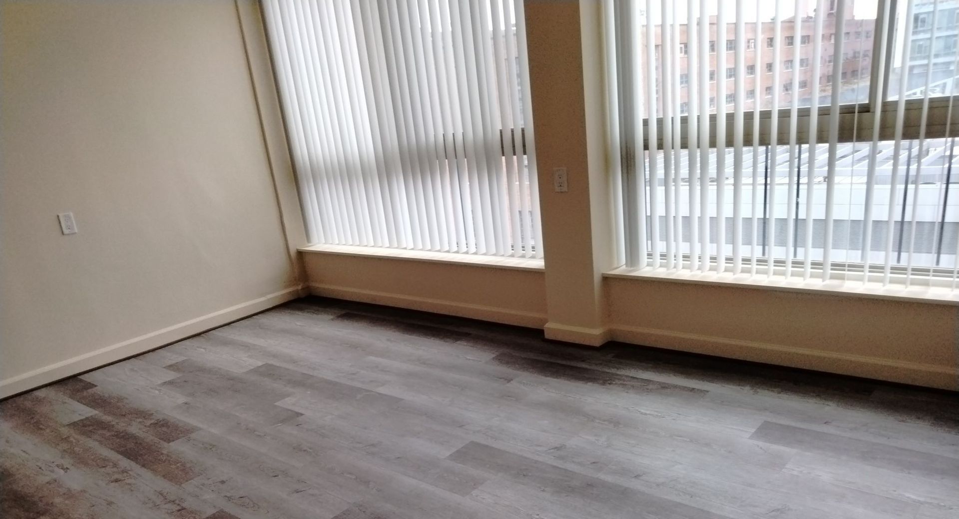 A living room with hardwood floors , blinds and a large window.