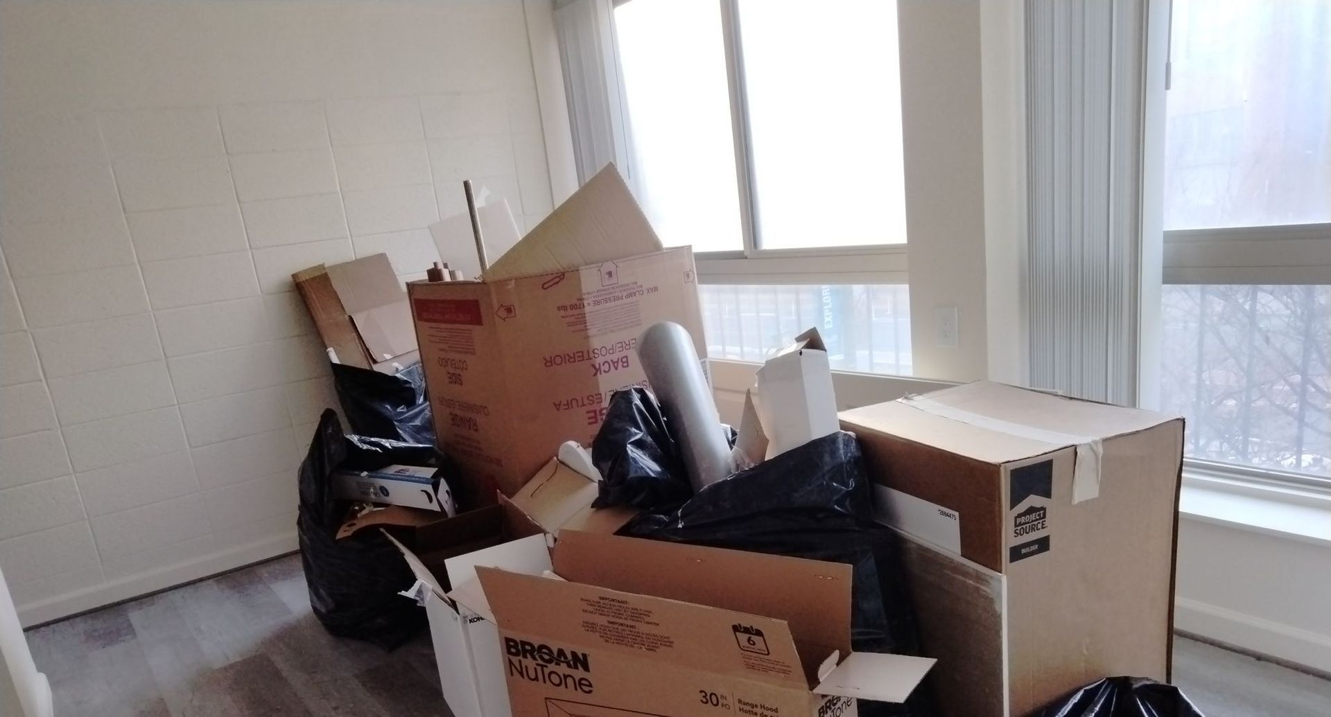 A room filled with boxes and trash bags in front of a window.