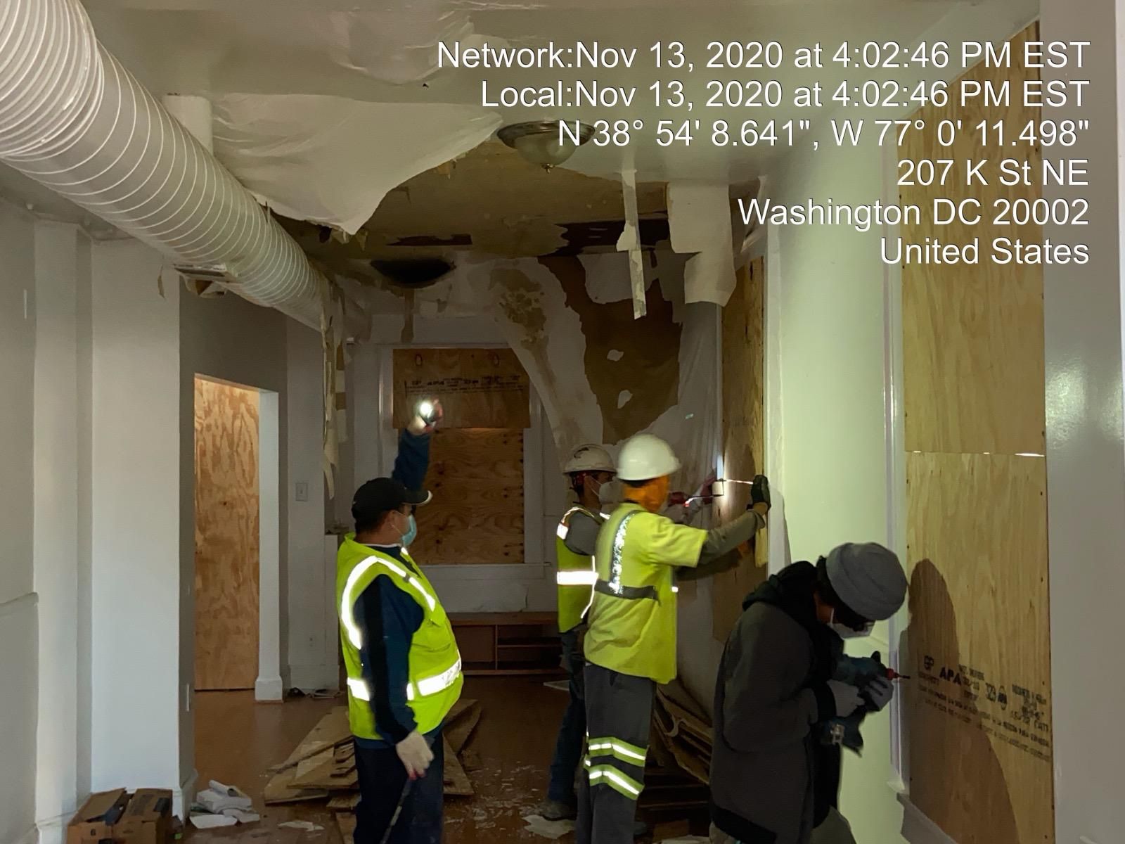 Construction workers inspecting damage in a building at 207 K St NE, Washington DC, with exposed walls and ceiling.
