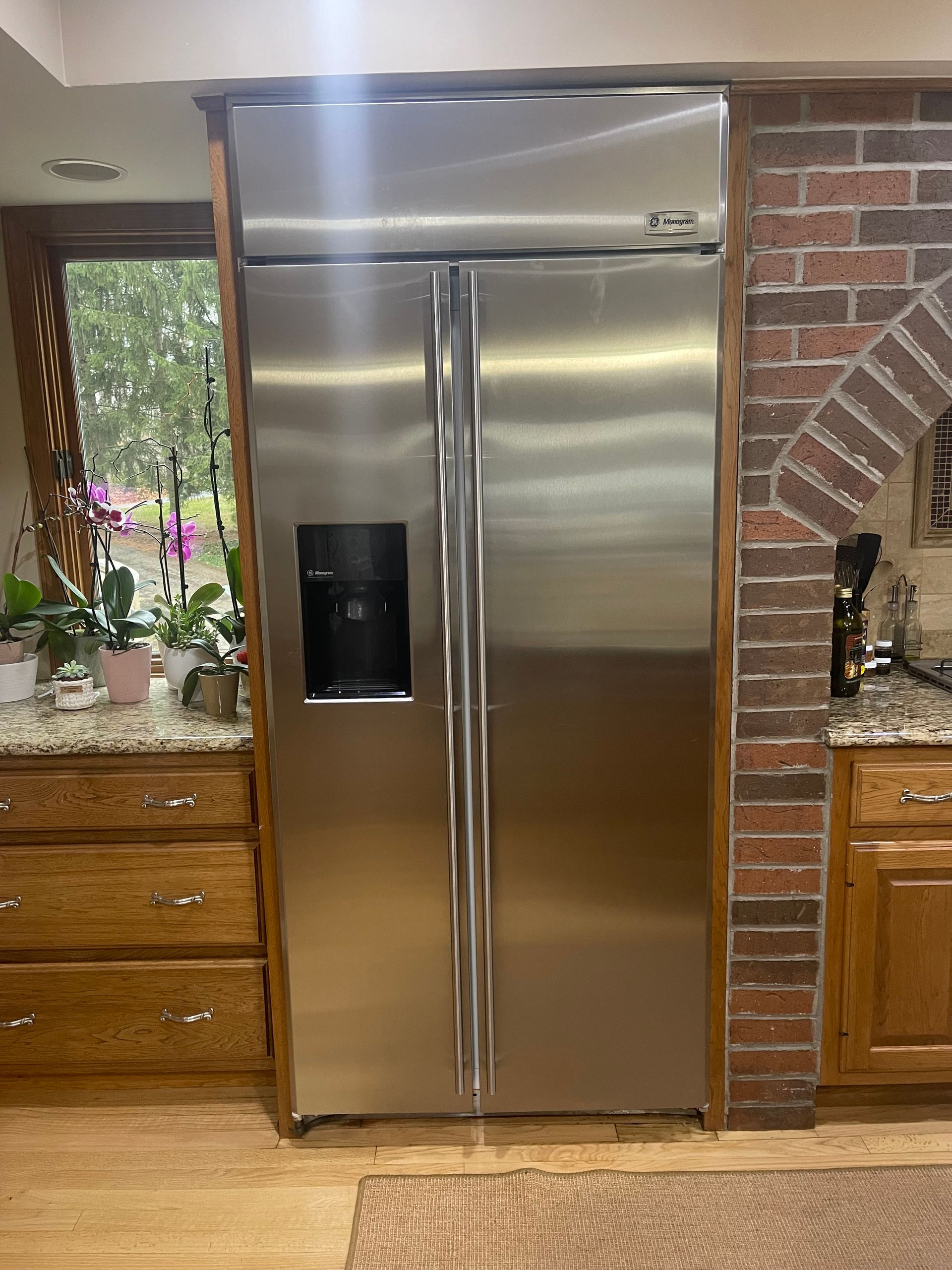 Stainless steel side-by-side refrigerator built into kitchen cabinetry, next to a brick wall.