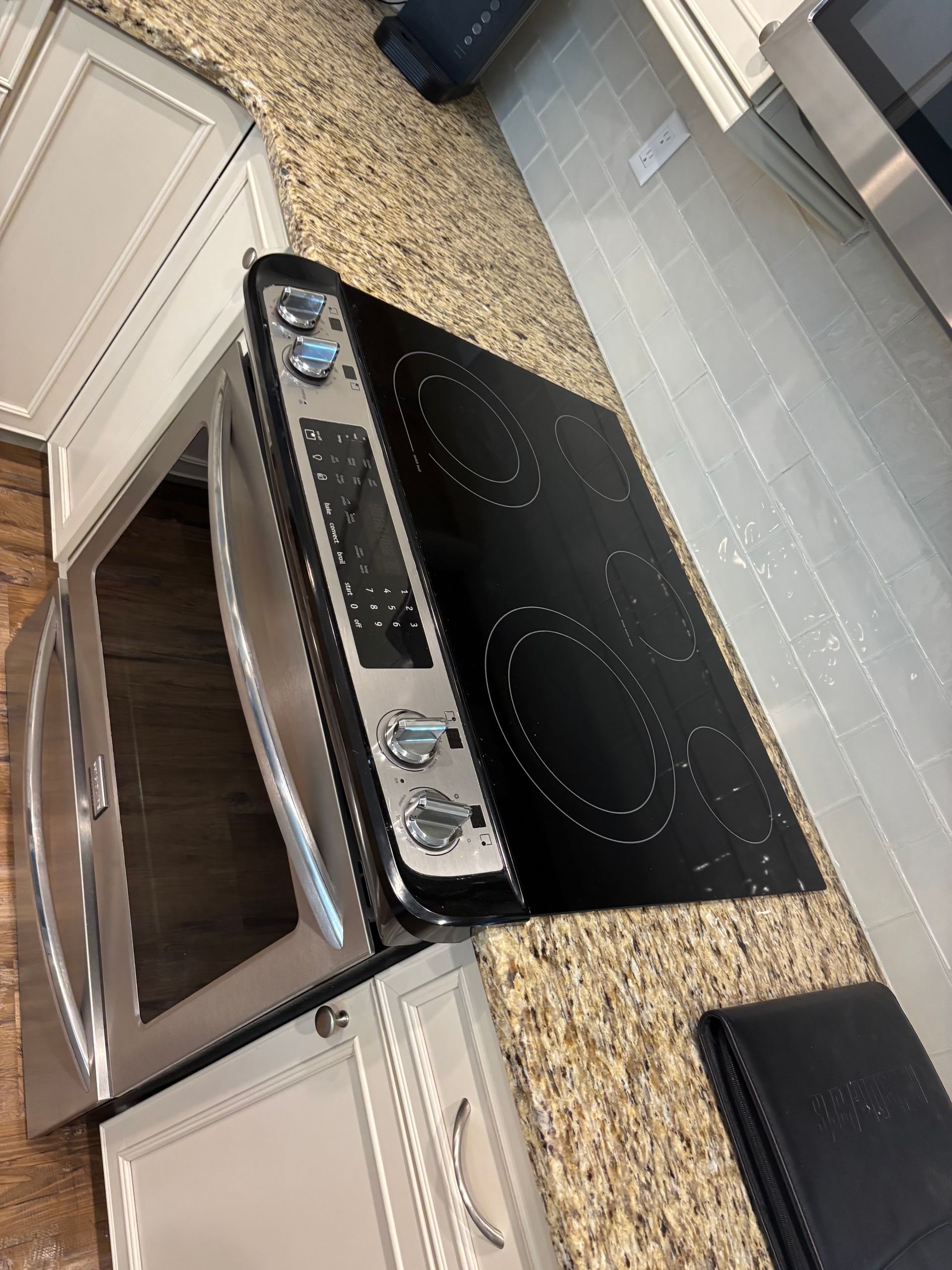 Electric stovetop next to a countertop oven, on a granite countertop in a kitchen.