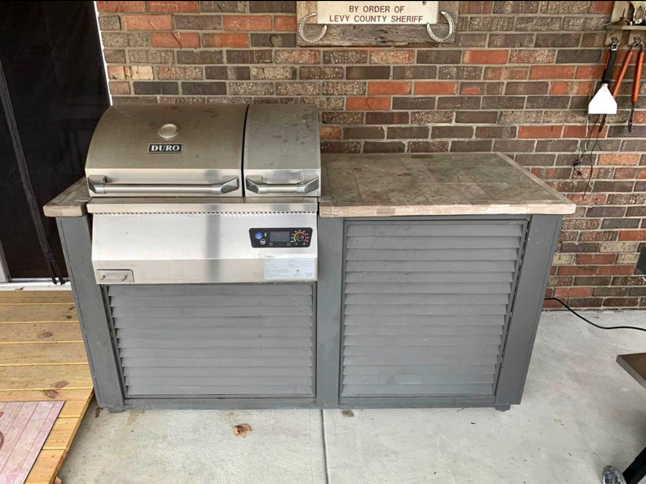 A stainless steel grill on a gray cabinet with a brown countertop sits on a concrete patio.