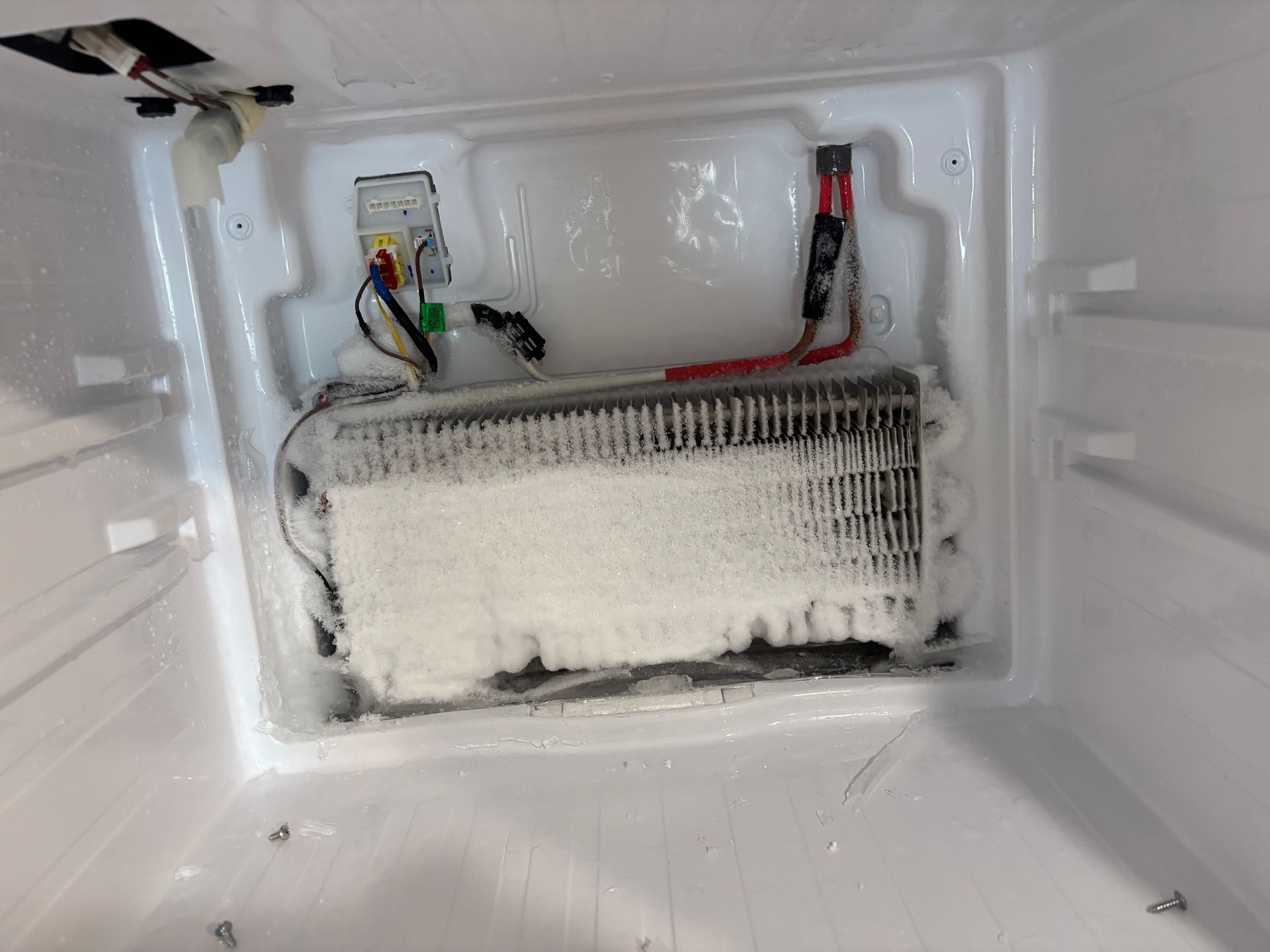 Inside a white freezer, a frosted coil is heavily coated with ice.