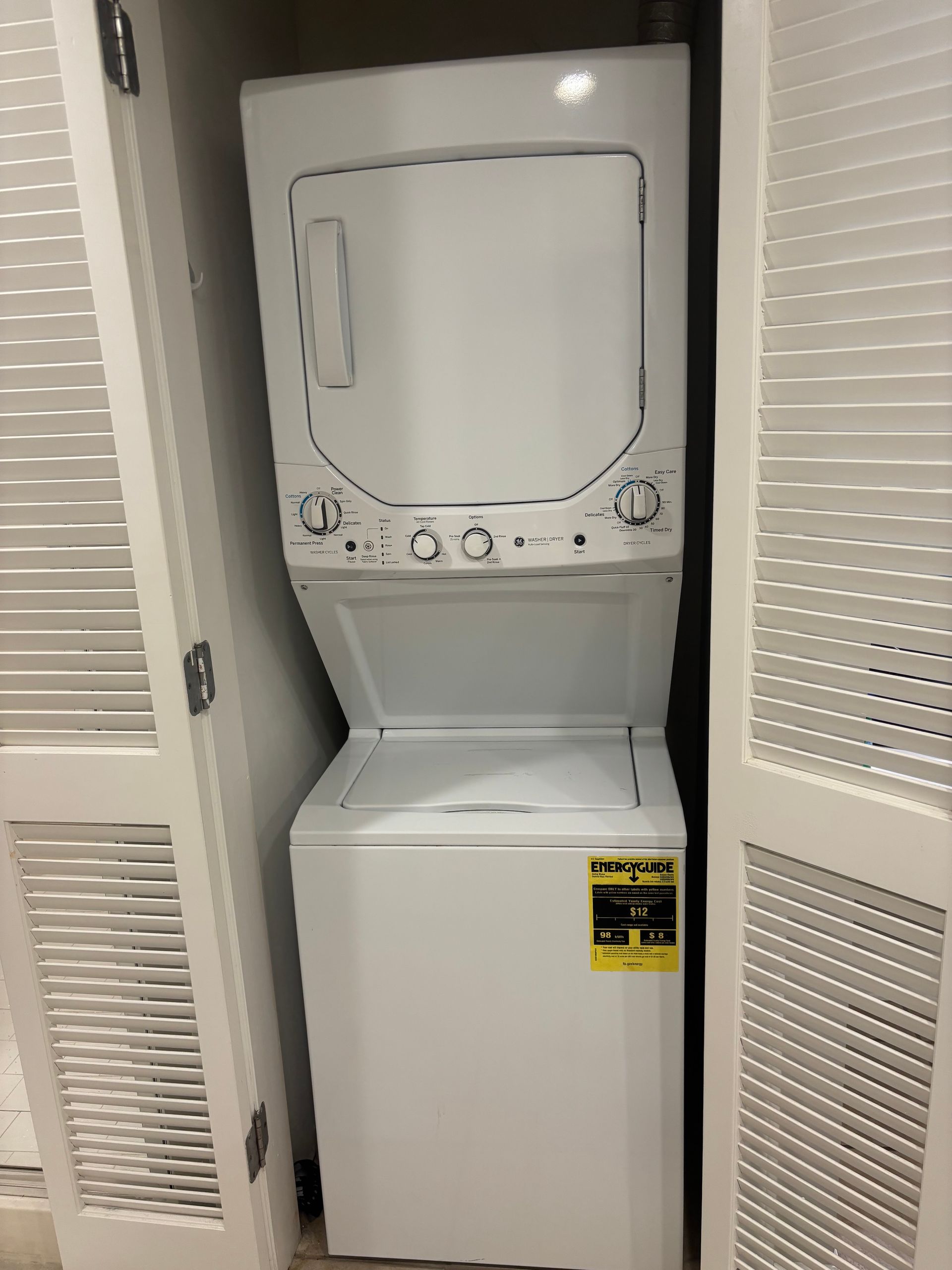 Stacked white washing machine and dryer in a closet, doors partially open.