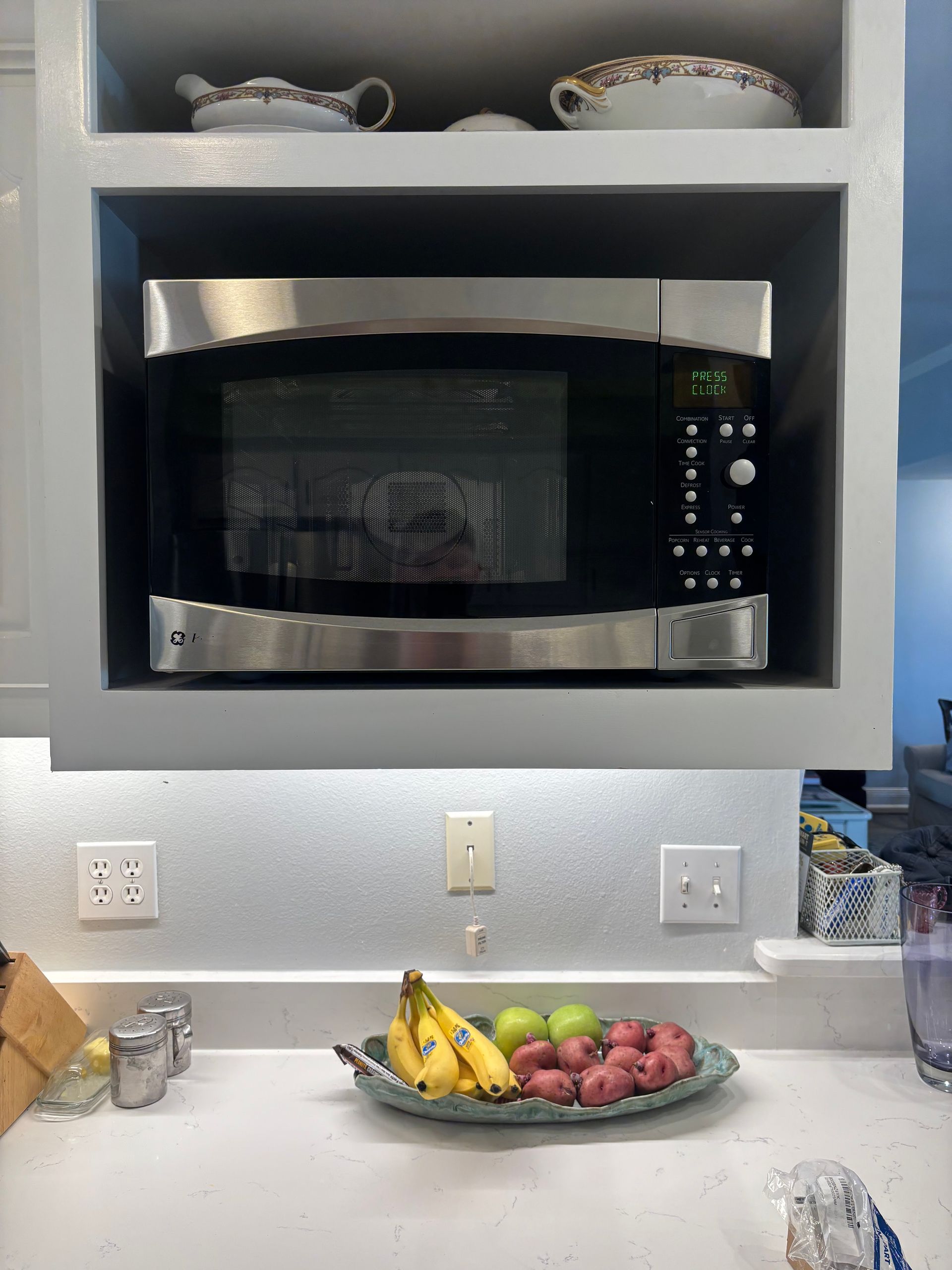 Microwave built into a cabinet above a counter with fruit.