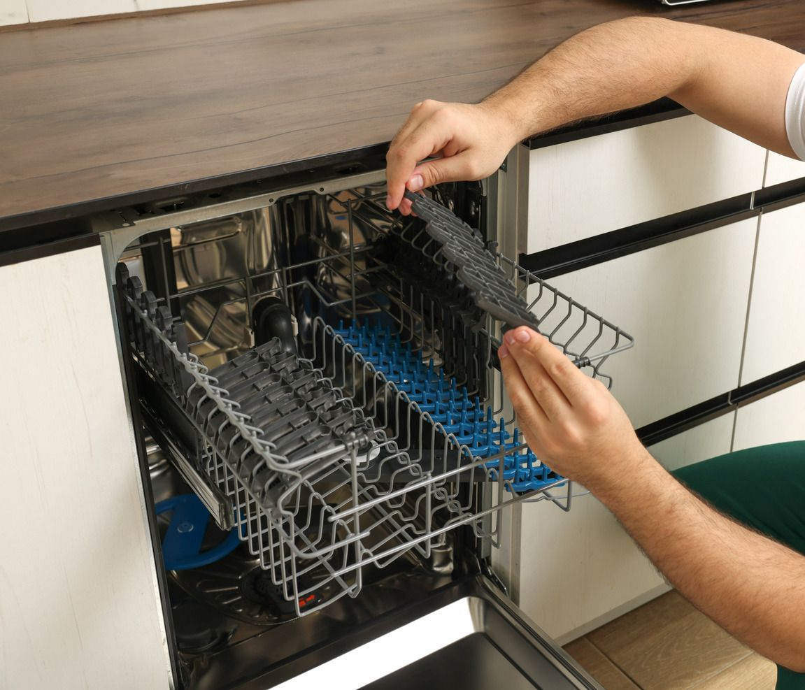 Person loading a dishwasher. Hands hold a rack of silverware. Interior shot.