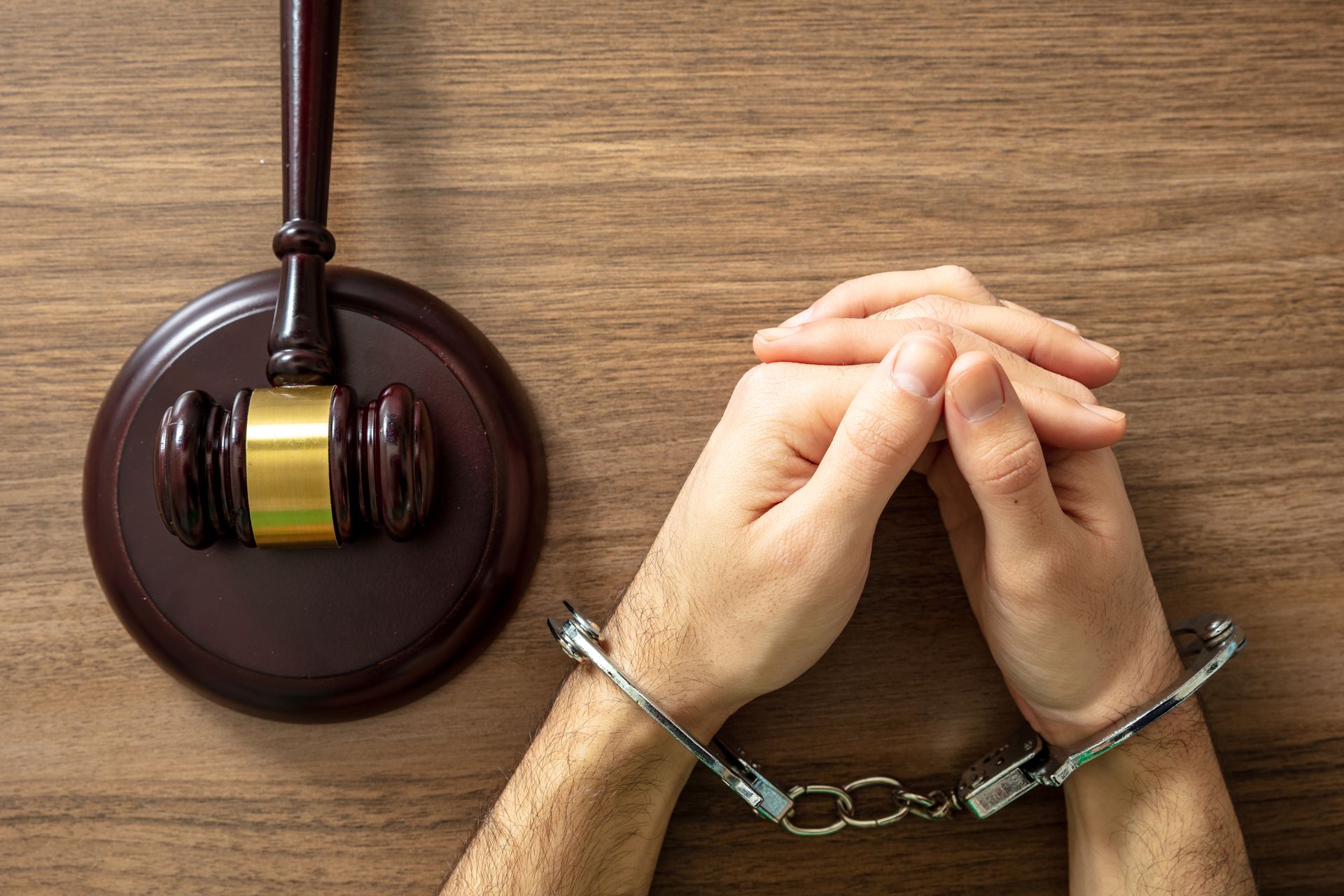 Hands in handcuffs next to a gavel on a wooden surface