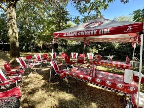 A group of red chairs and tables under a canopy in a park.