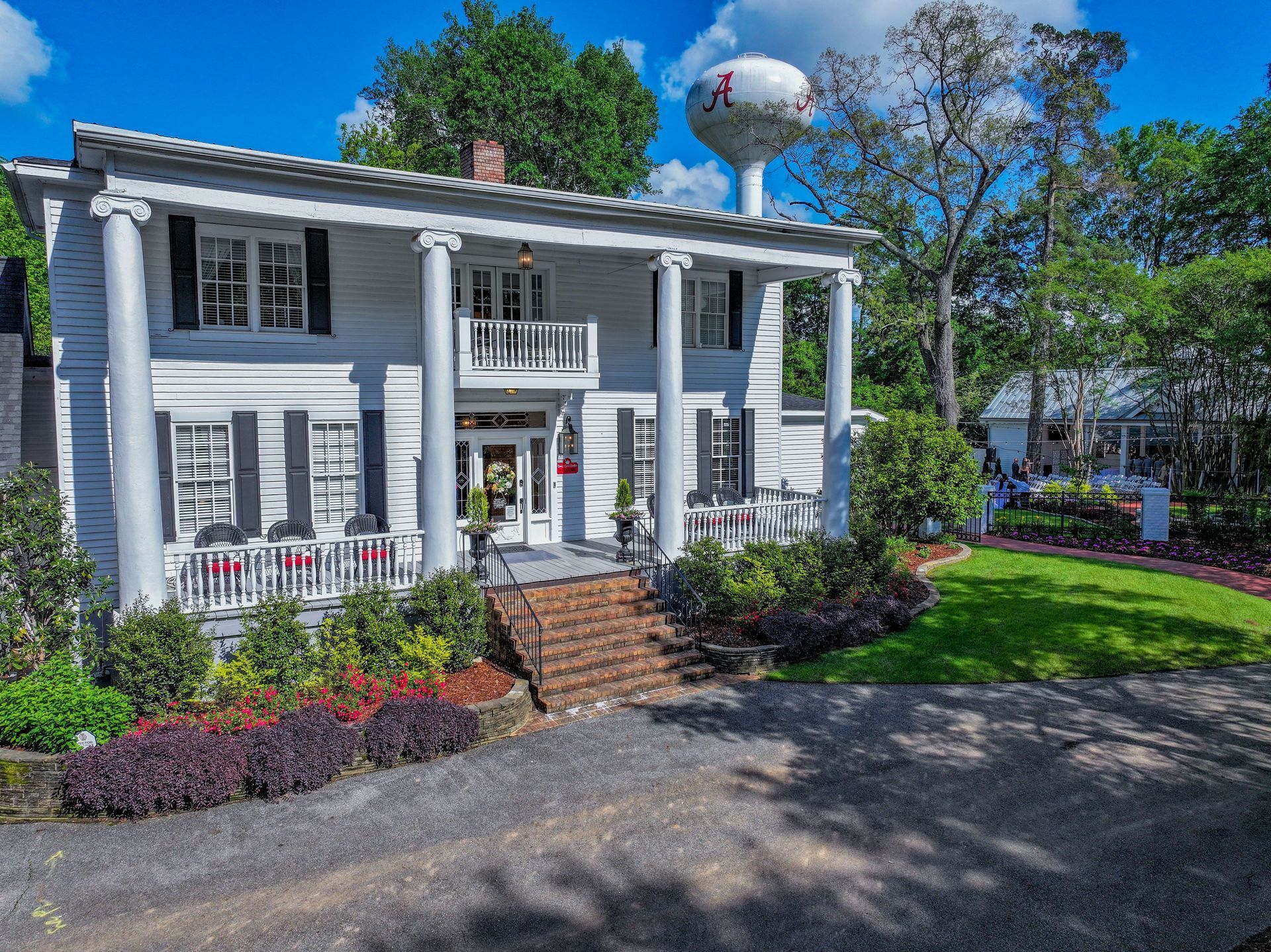 A large white house with a large porch is surrounded by trees.