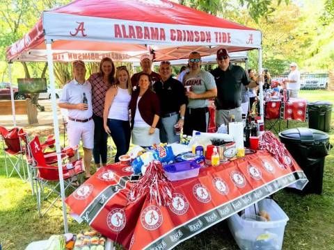 A group of people are posing for a picture in front of an alabama crimson tide tent.