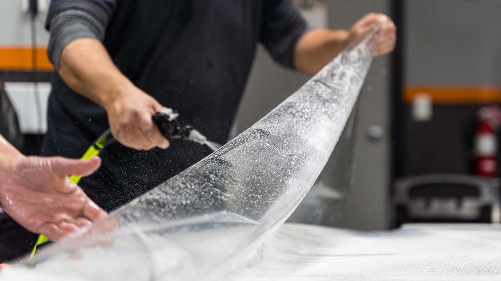 Hands spraying liquid over a translucent sheet on a worktable in a workshop