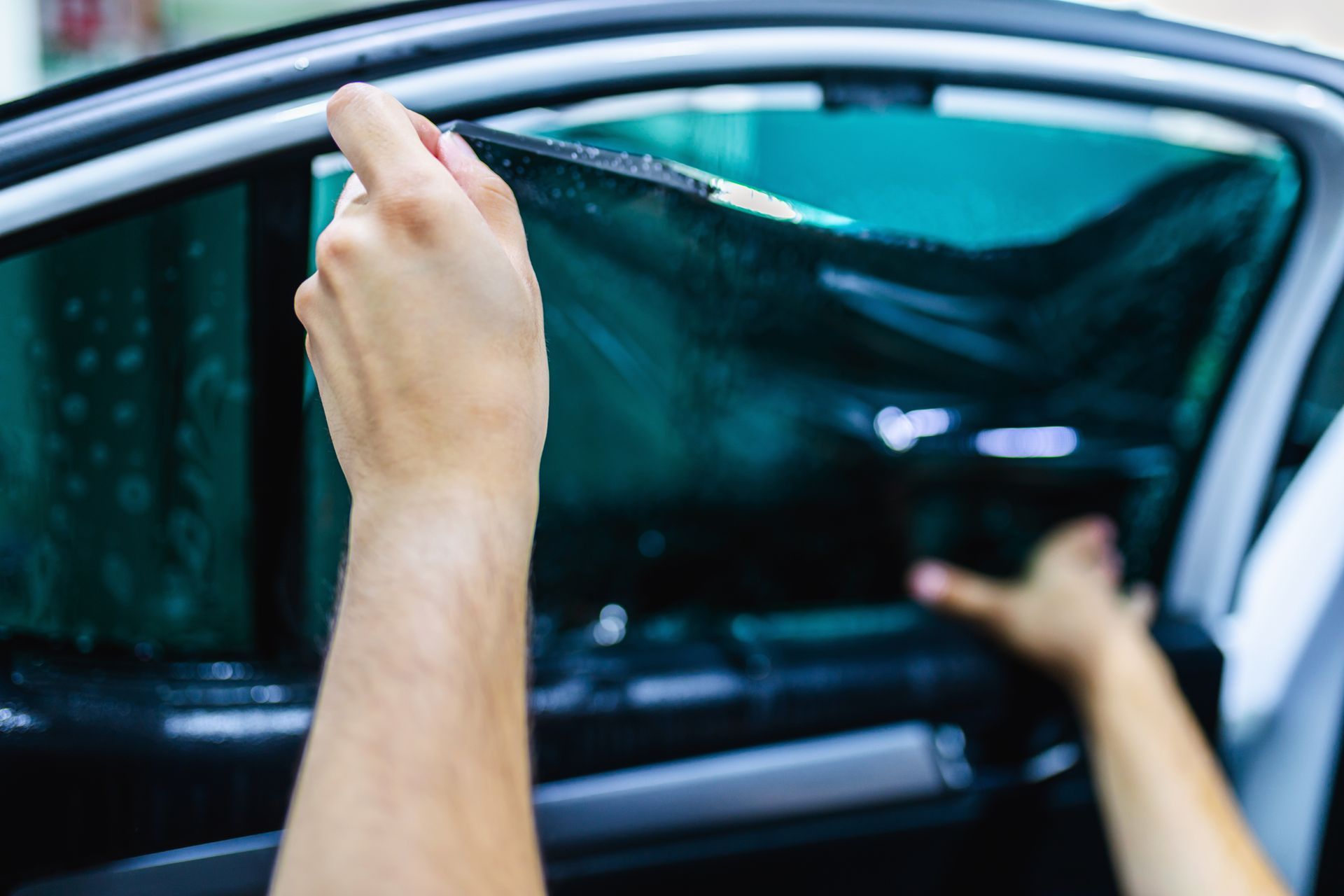 Hands peel a car window tint film from a blue car door.