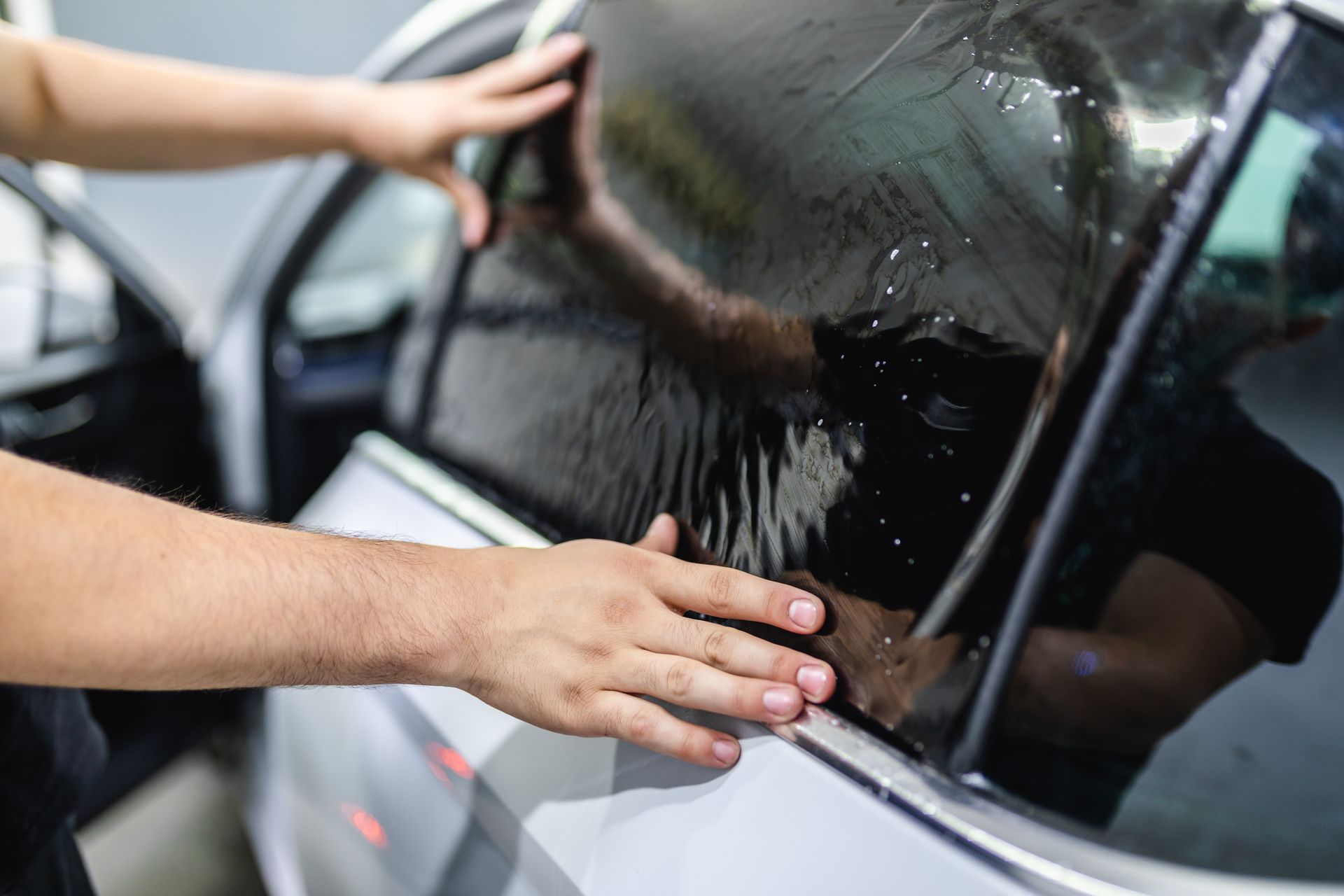 Hands wiping water off a black car window with a cloth