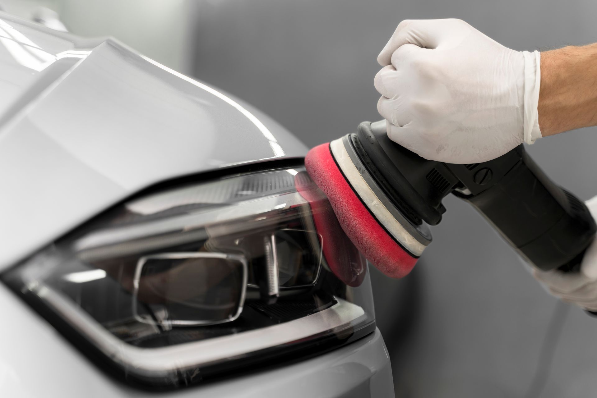Car detailer polishing a silver car headlight with a buffing machine