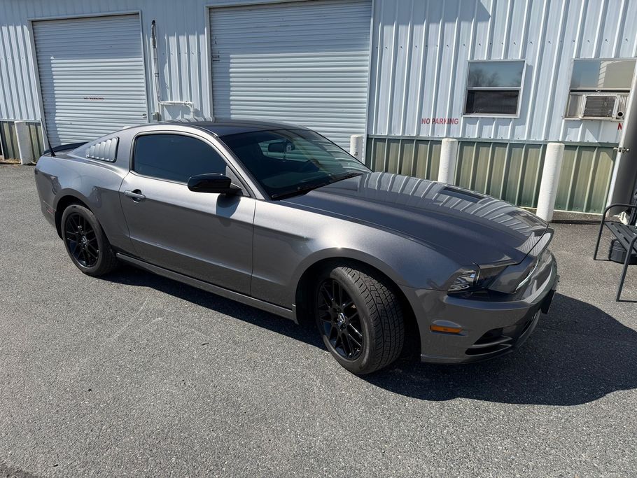 Gray sports coupe parked in front of a corrugated metal building with closed garage doors.