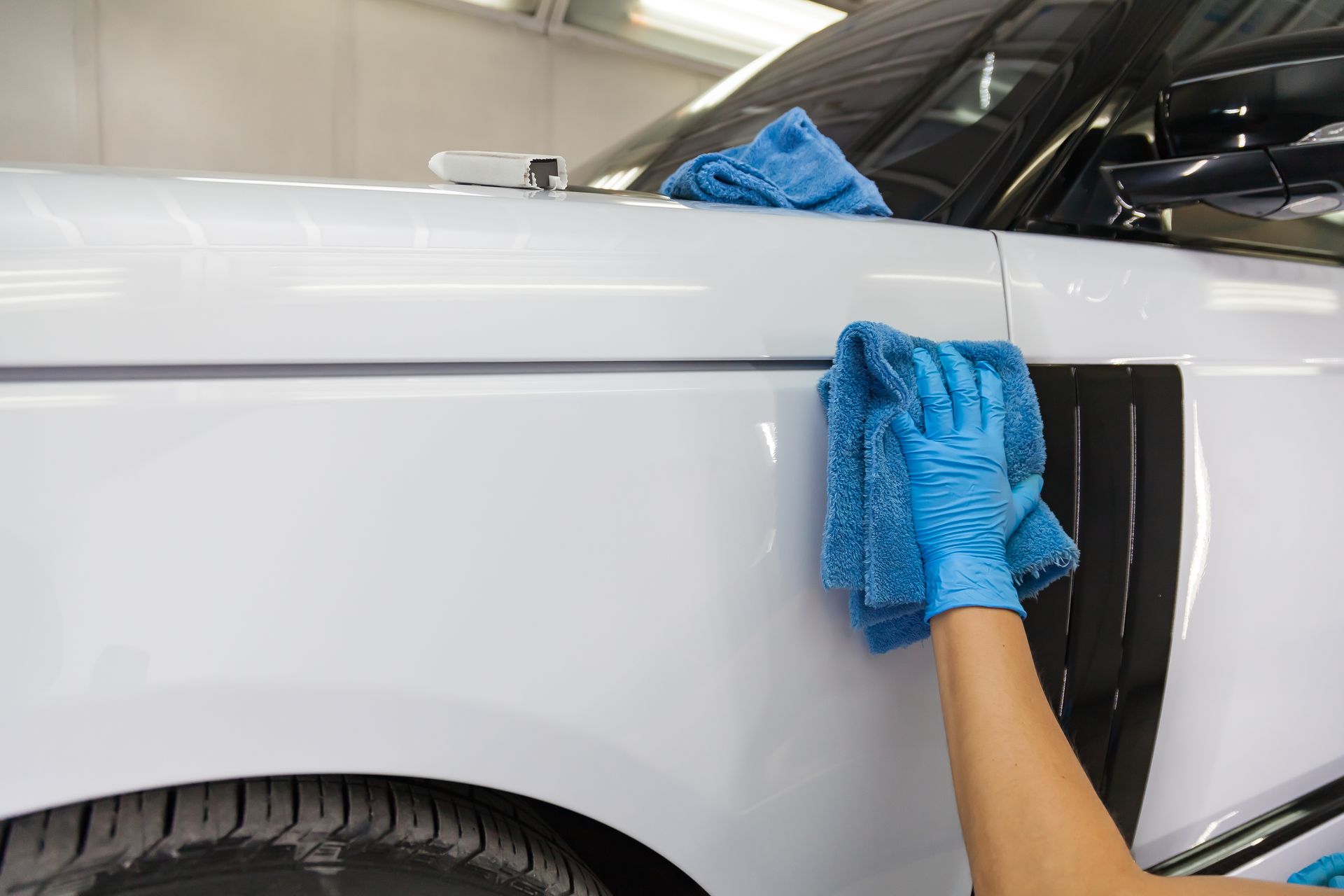 Hand cleaning a white car’s side panel with a blue microfiber cloth in a garage
