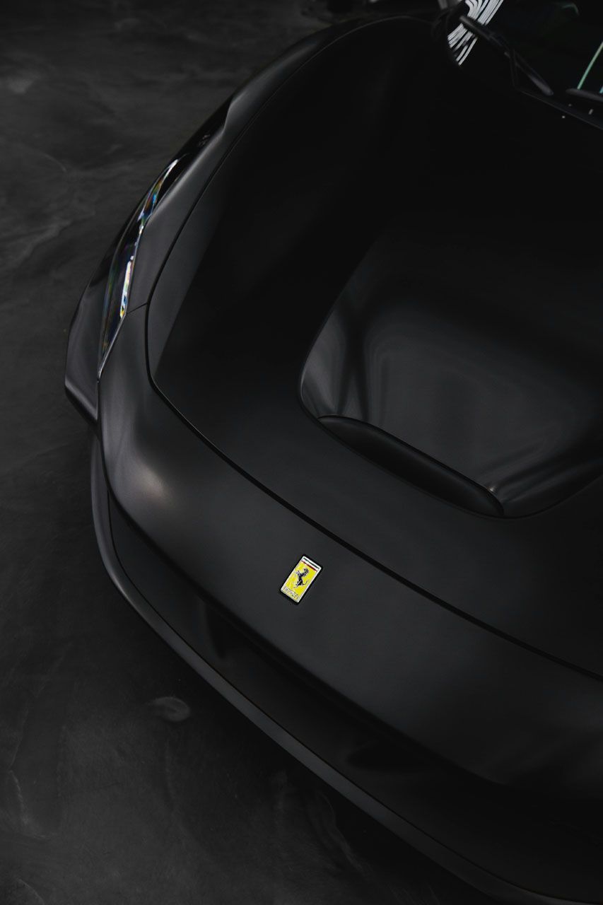 Black Ferrari sports car front hood with yellow emblem, viewed from above on a dark floor