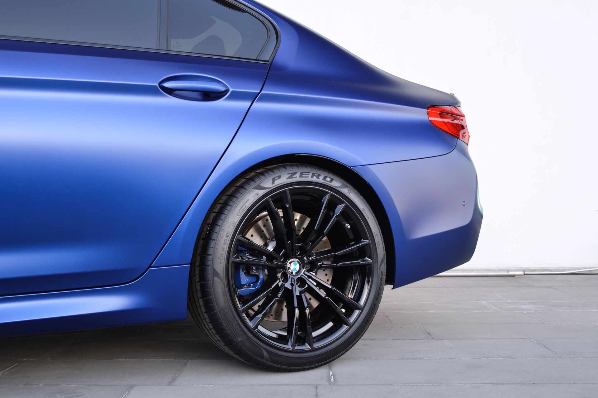 Blue sports sedan rear side view with black alloy wheel on a gray floor against a white wall