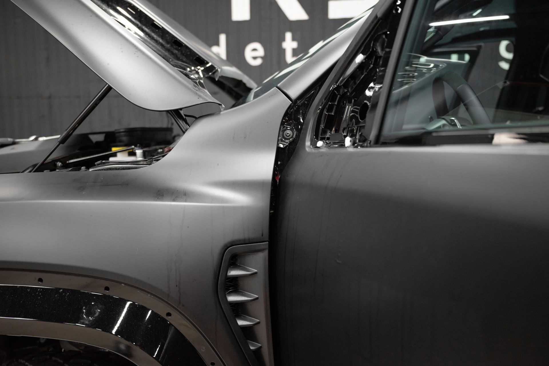 Close-up of a matte gray car with hood open and a door ajar in an indoor showroom