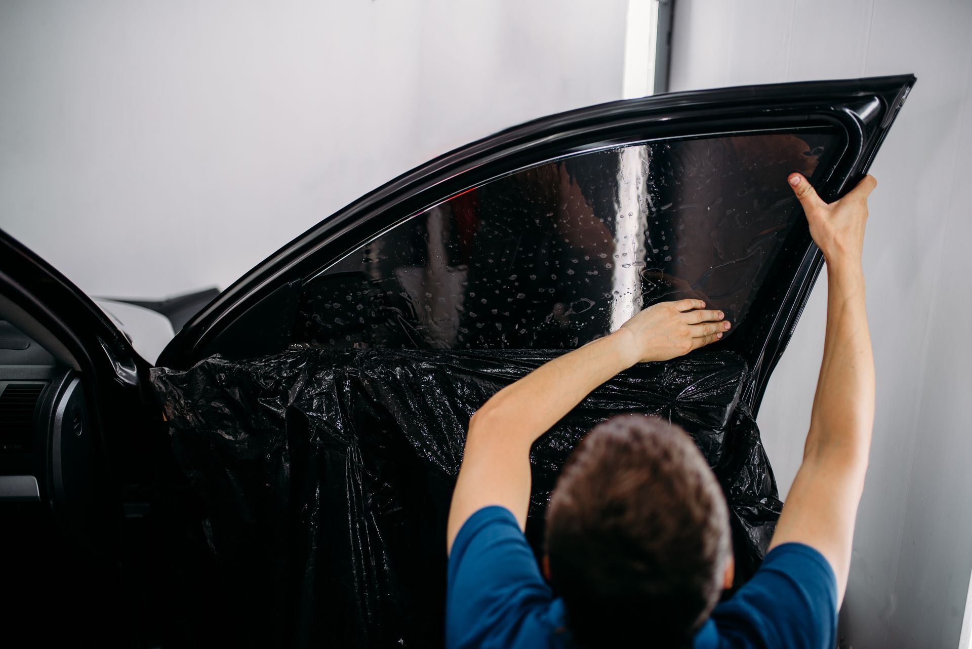 Person washing a black car door with water spray outdoors