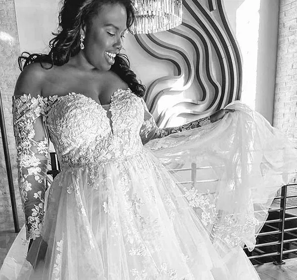 Woman in a wedding dress smiles, holding up the skirt. Indoors with modern art and natural light.