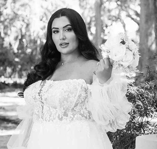 Bride in white gown holding bouquet, outdoors.