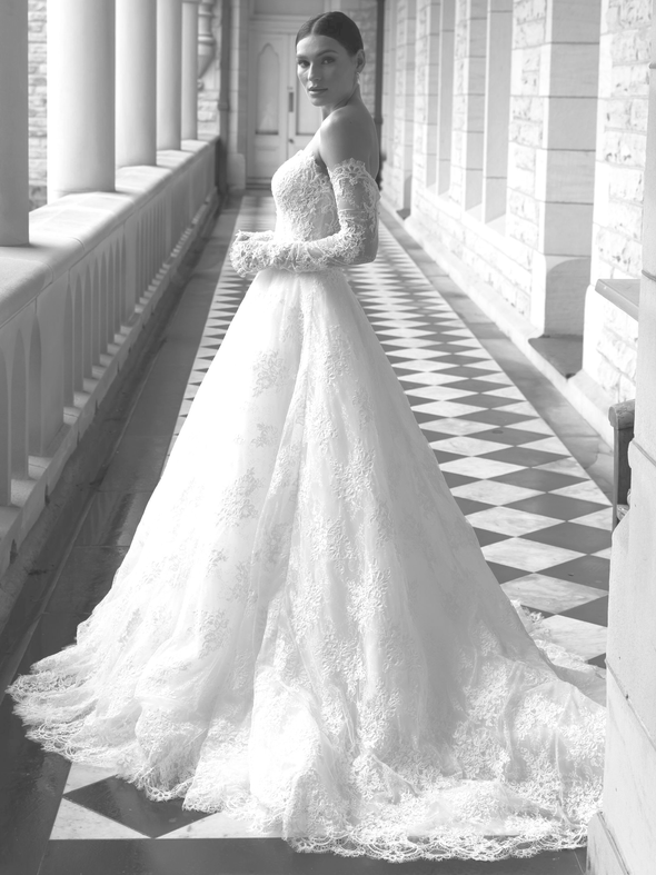 Woman in white wedding dress, open back, posing on balcony with trees.