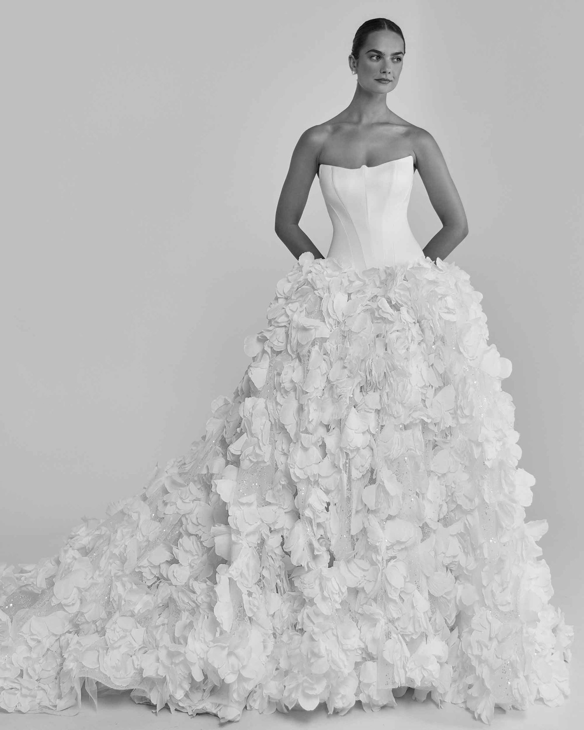 Woman in a strapless white wedding gown with a heavily layered, textured skirt, standing.