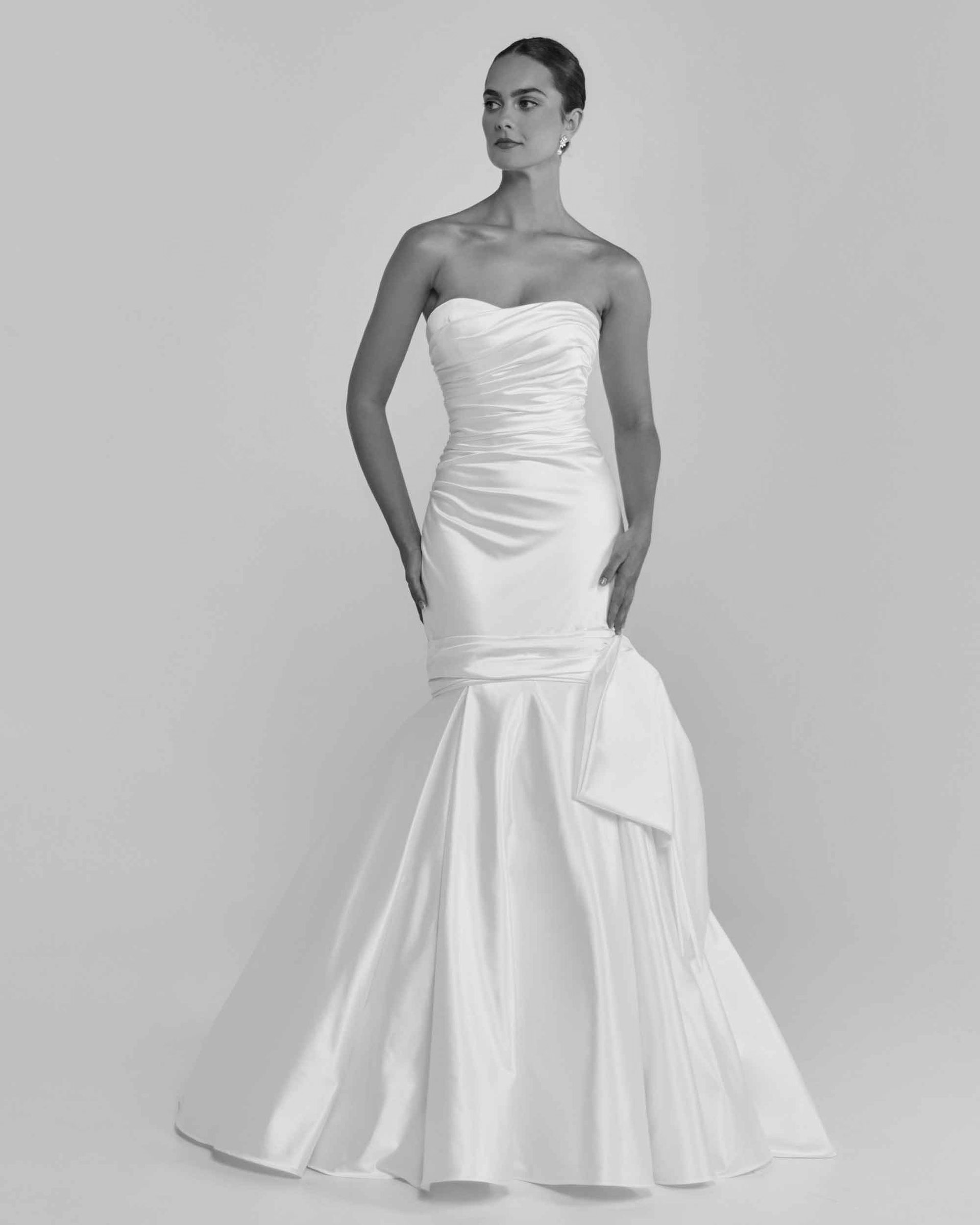 Woman in strapless white mermaid wedding dress, hands at sides, in studio.