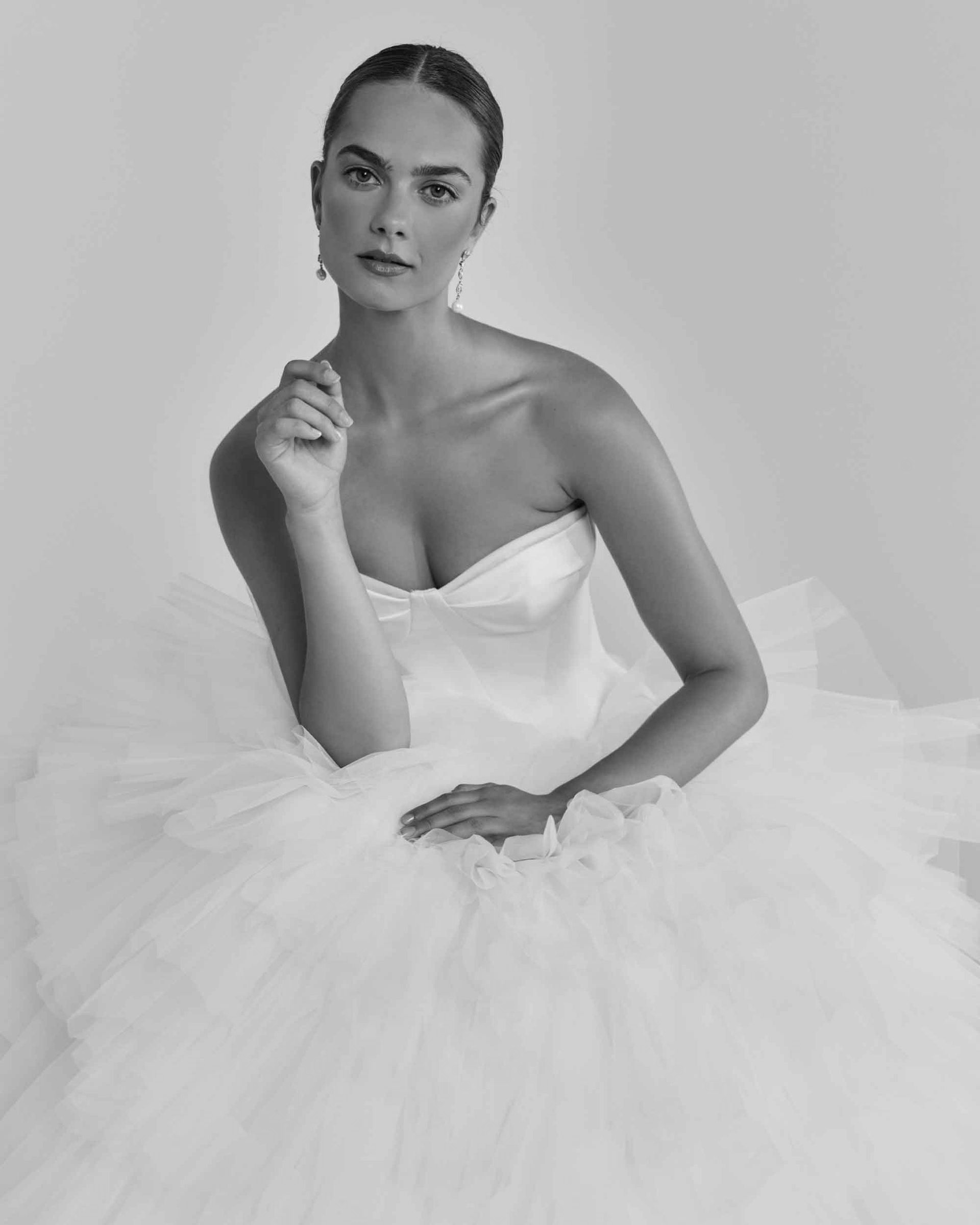 Woman in a strapless white wedding dress, resting her arm, looking at the camera.