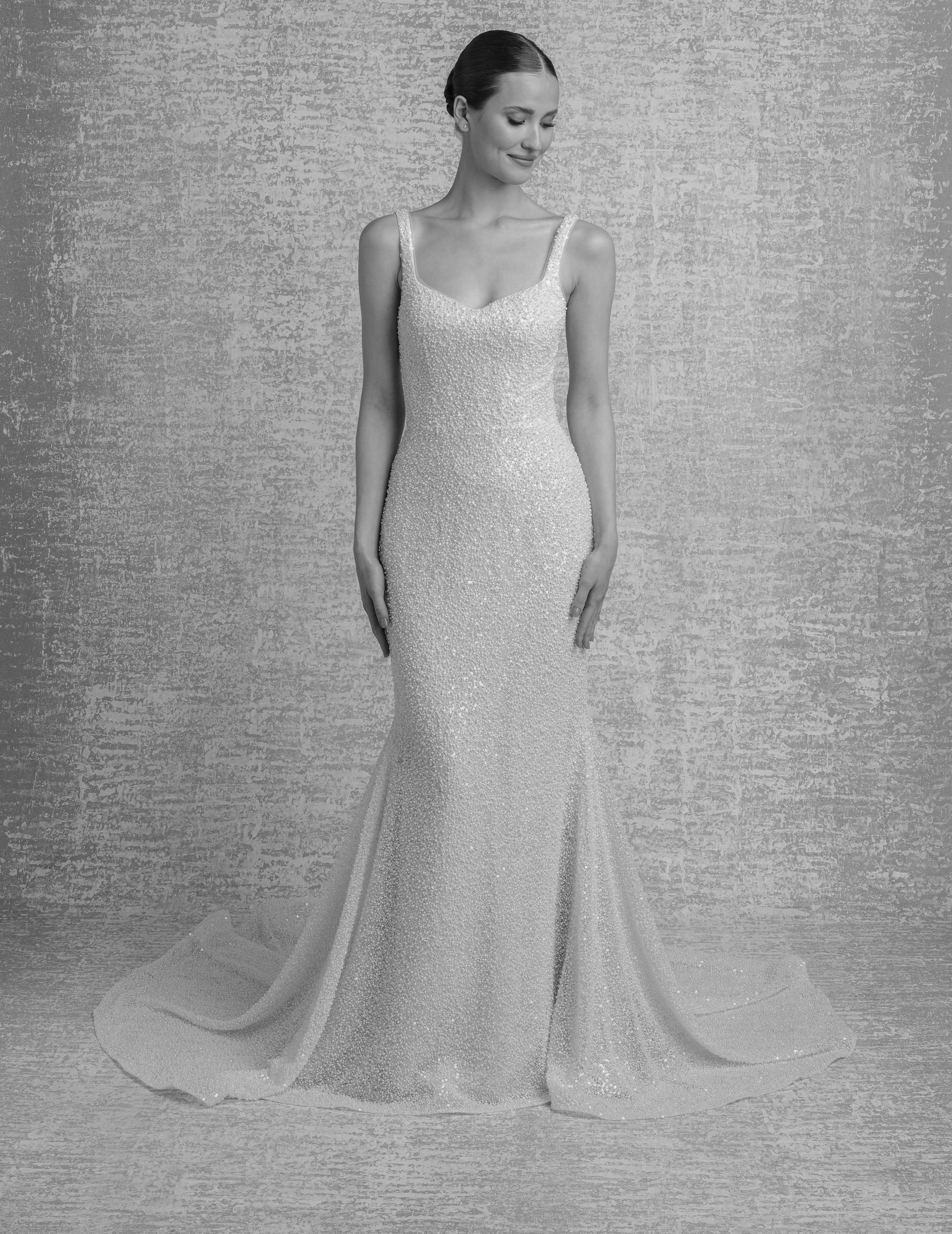 Woman in a sparkly, fitted wedding dress with a train, against a textured backdrop.