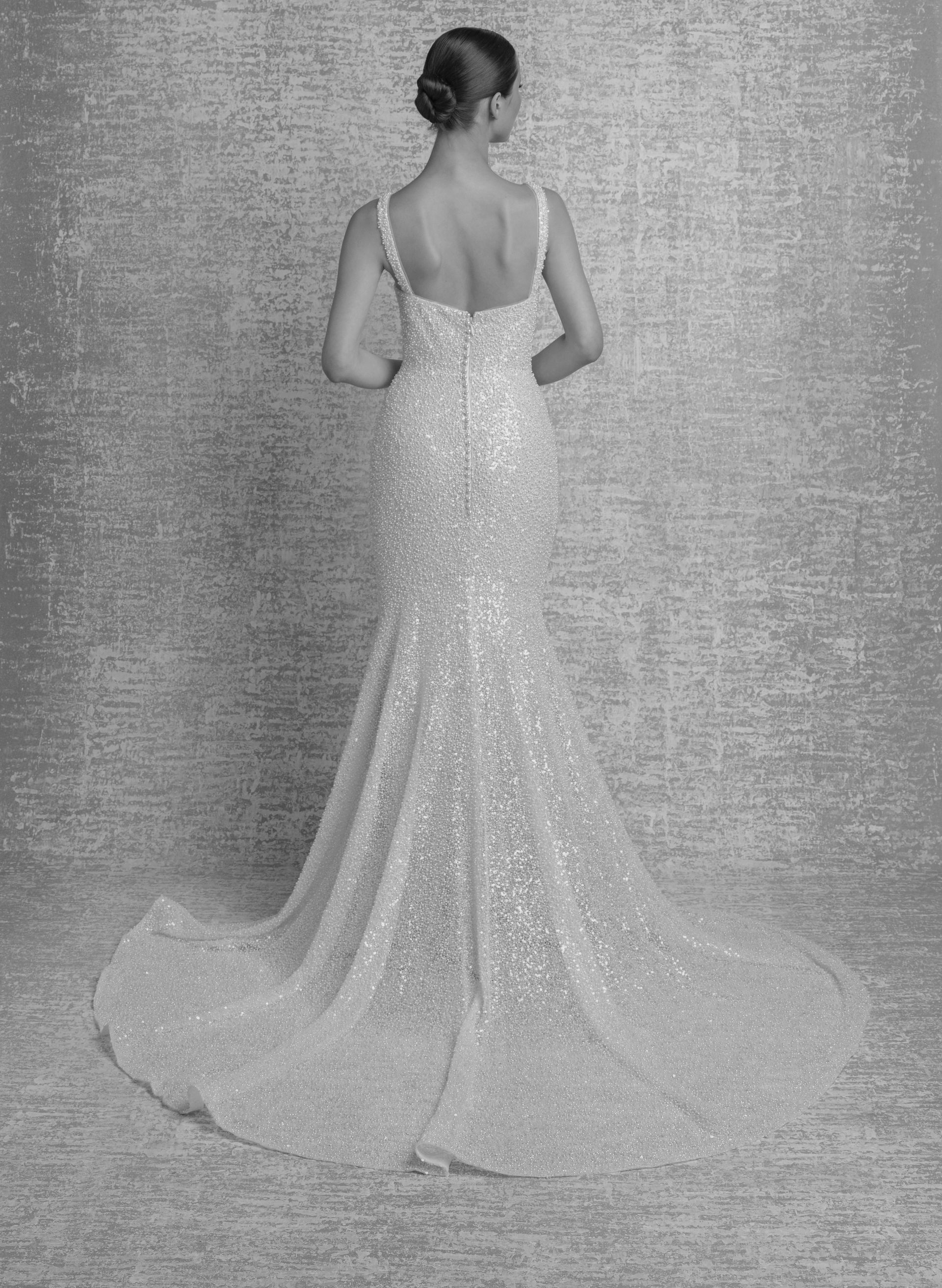 Woman in a sequined wedding dress, back view, standing on a textured background.