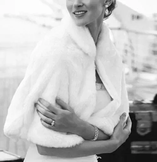 Bride in white fur shawl, smiling, with a diamond ring and bracelet.
