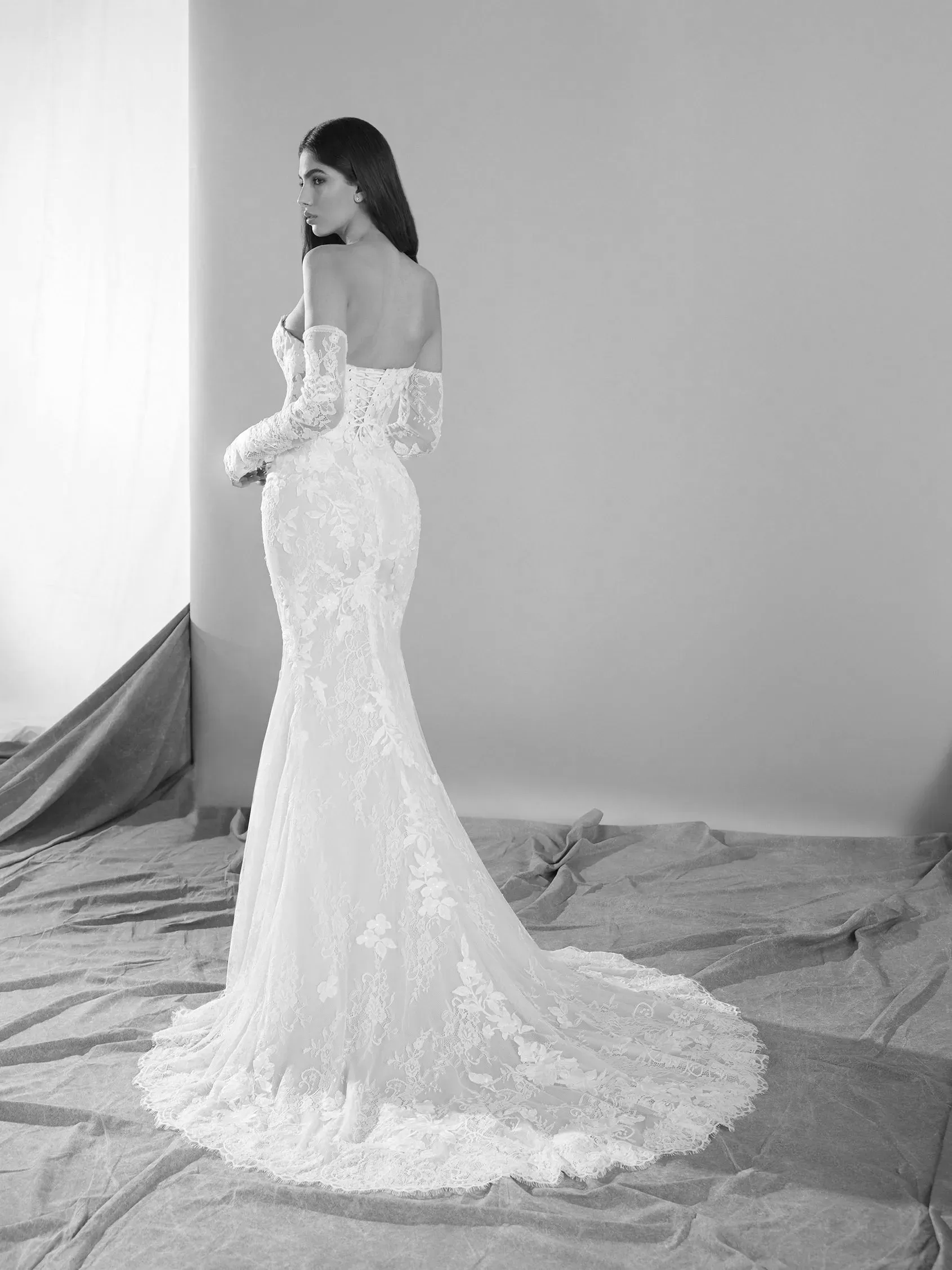 Woman in a lace wedding dress with long sleeves, standing with back to camera.
