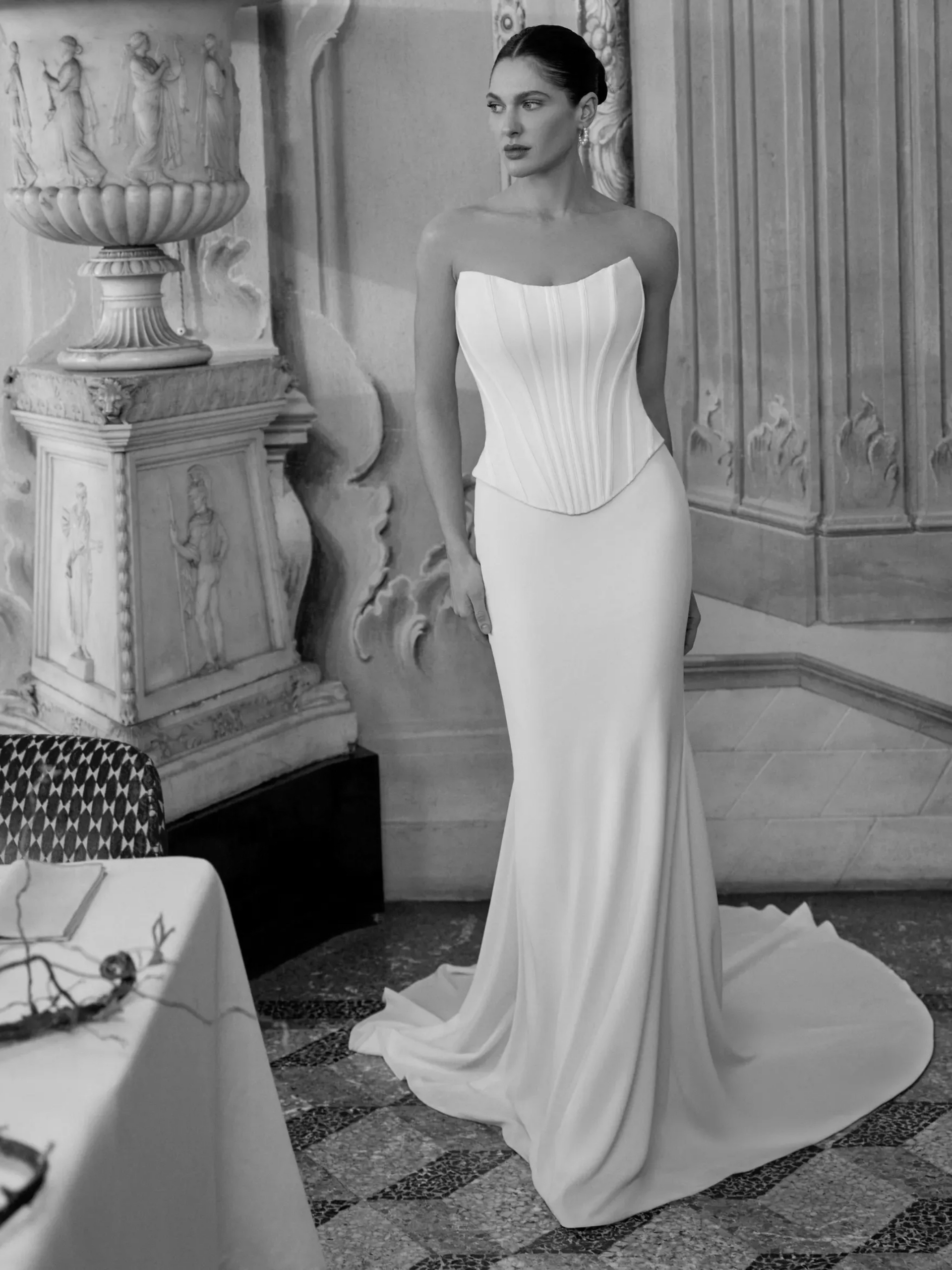 Woman in a white corset wedding dress with a train, standing indoors.