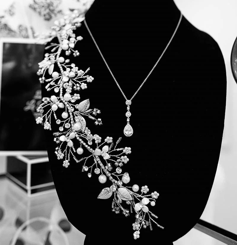Silver floral headpiece and teardrop pendant necklace on black velvet display.