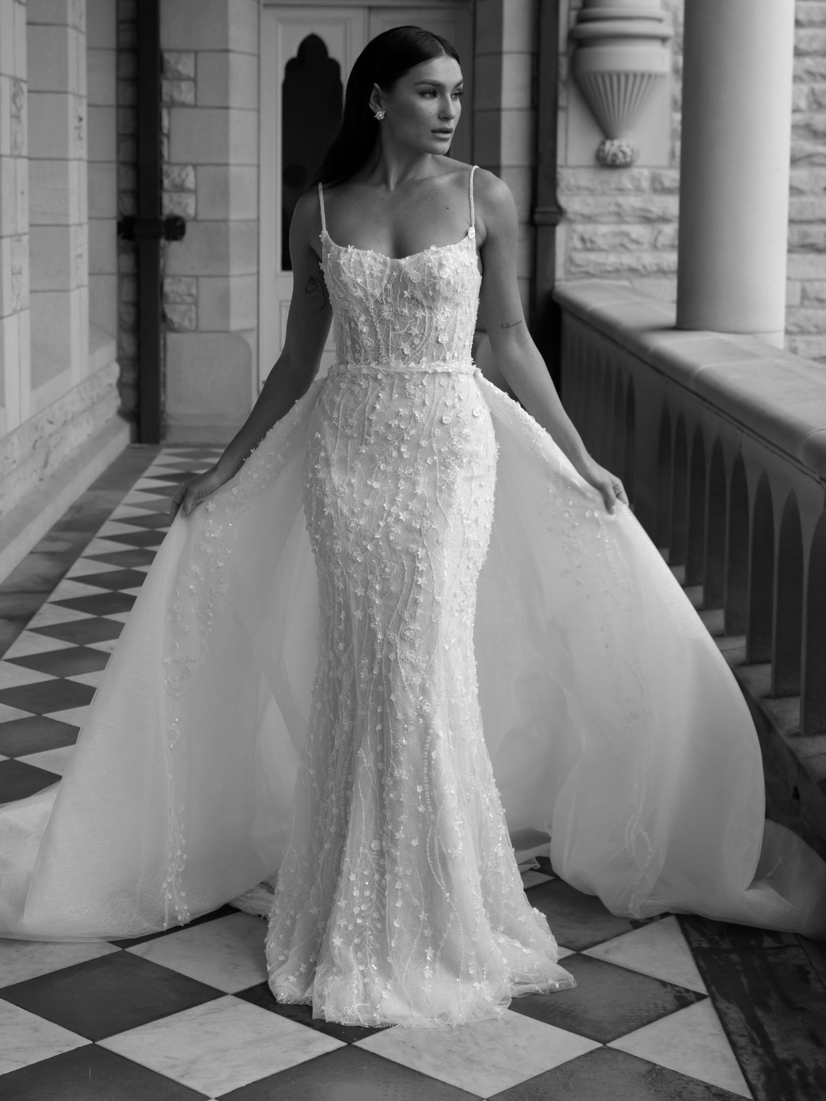 Woman in embellished wedding dress with a detachable train, standing on a patterned stone walkway.
