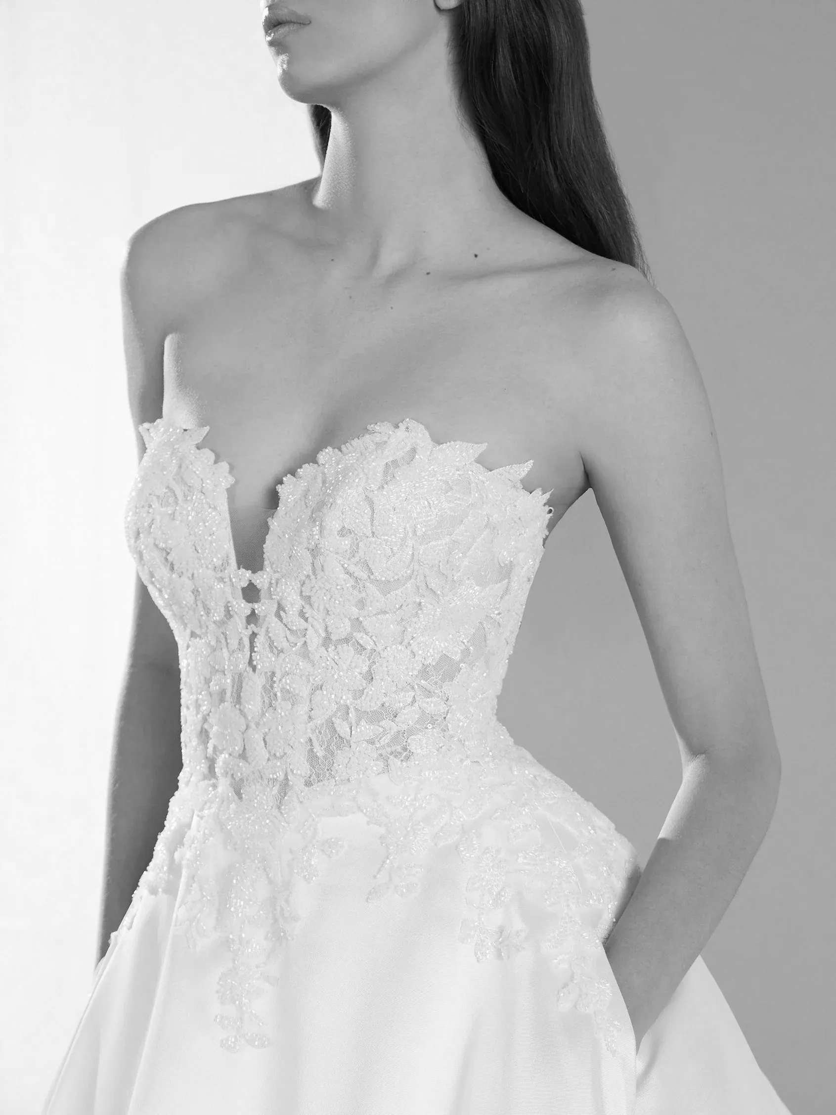 Woman in strapless, lace wedding dress with a plunging neckline, hands in pockets.