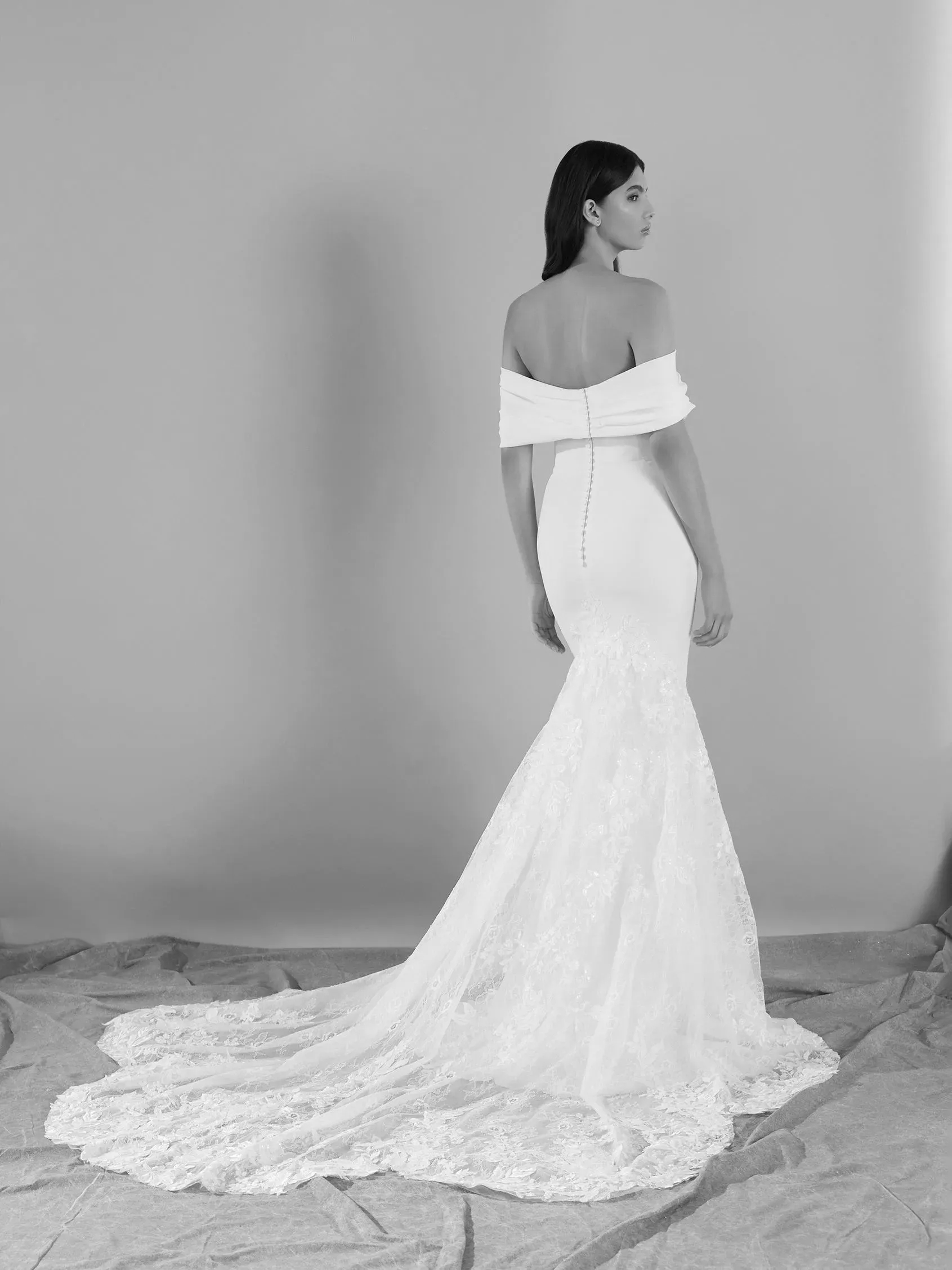 Woman in white off-the-shoulder wedding dress, back view, posing, long train, studio setting.