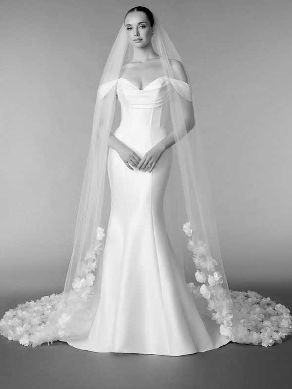 Three women in a bridal shop. One bride tries on a dress, veil adjusted by two assistants.