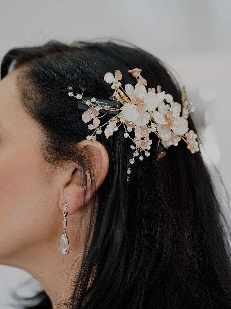Woman with dark hair wearing a floral hair comb, earrings, and dark clothing.