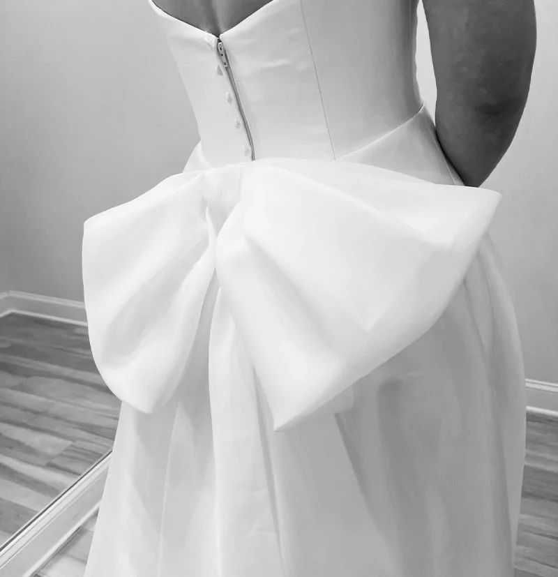 Woman in a white dress with a large bow detail on the back; indoors.