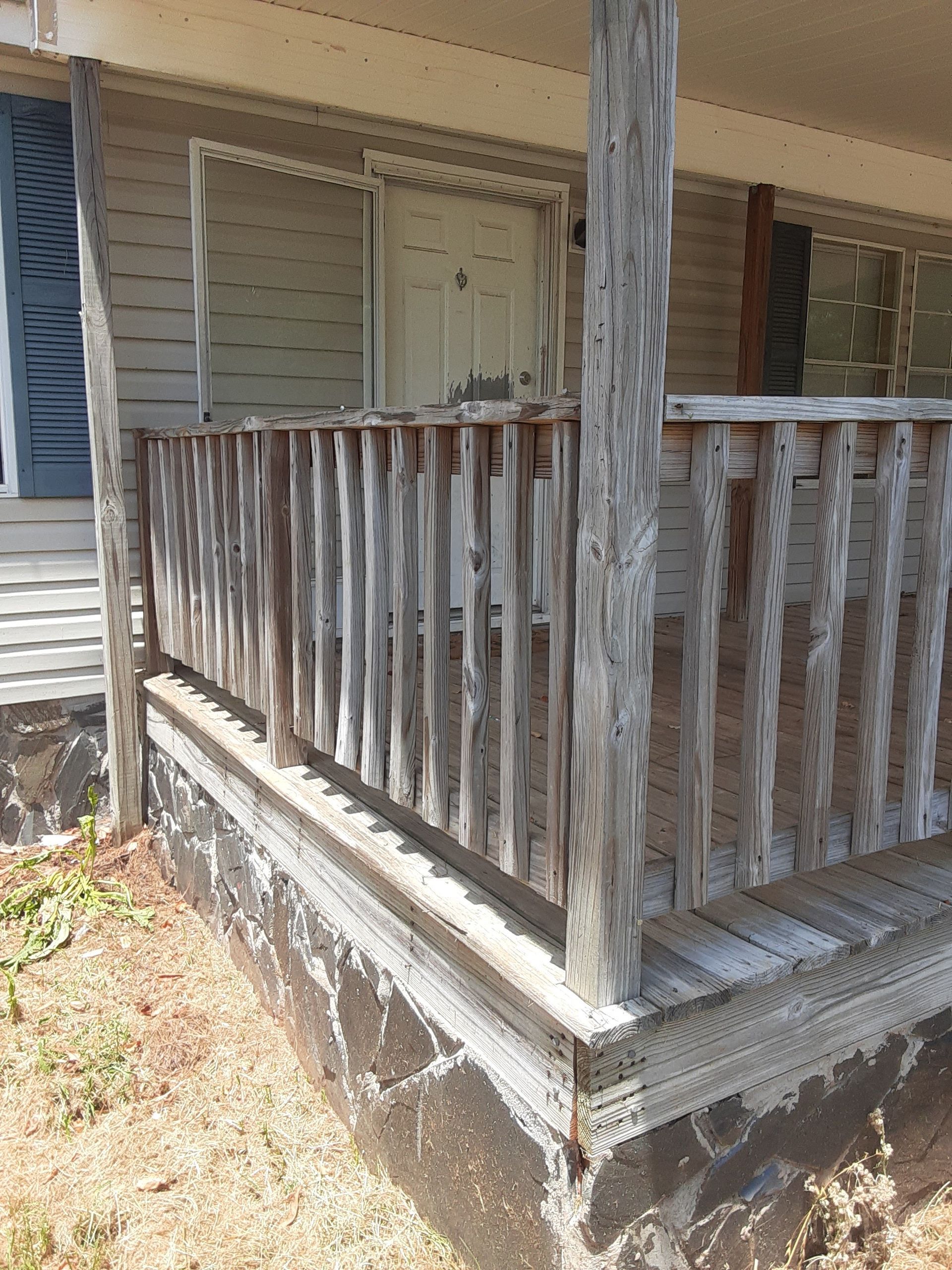 A porch with a wooden railing and a gray house in the background.